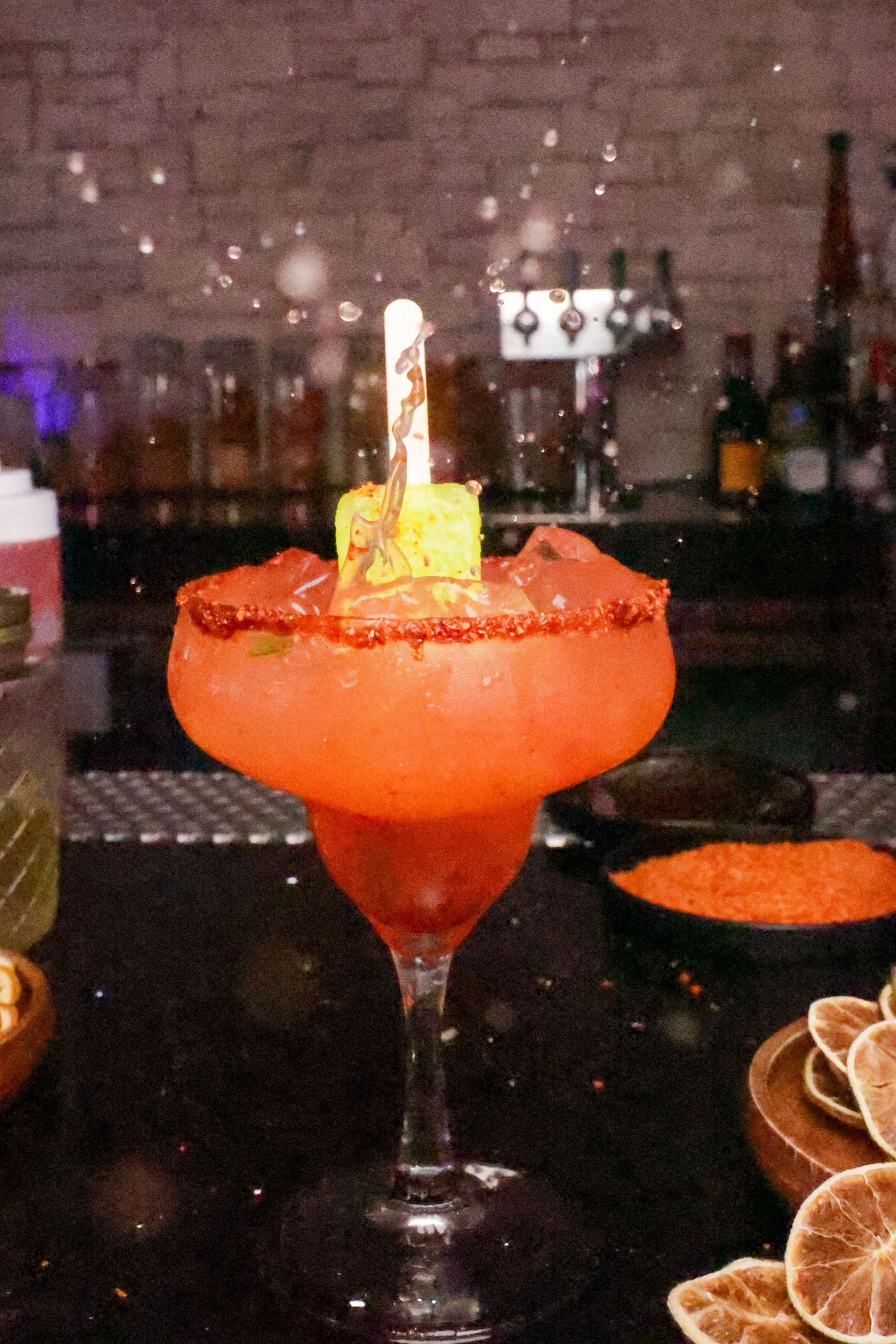 Flaming orange cocktail with salt rim and citrus garnish in a dramatic bar setting.