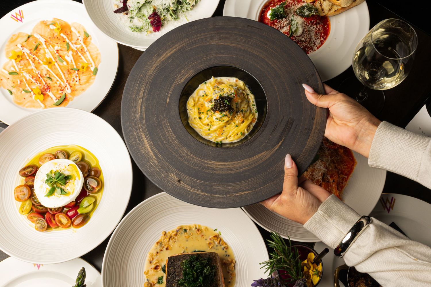 Aerial view of multiple gourmet dishes arranged on a dark restaurant table.
