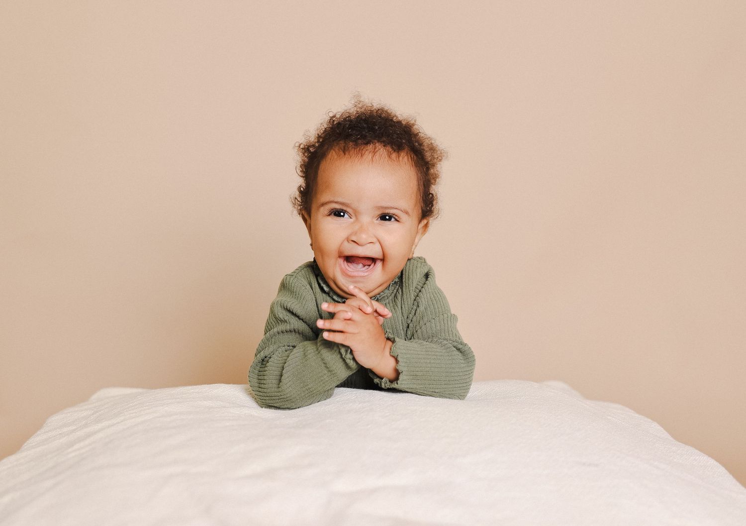 Child peeking over white bedding with playful expression in studio setting.