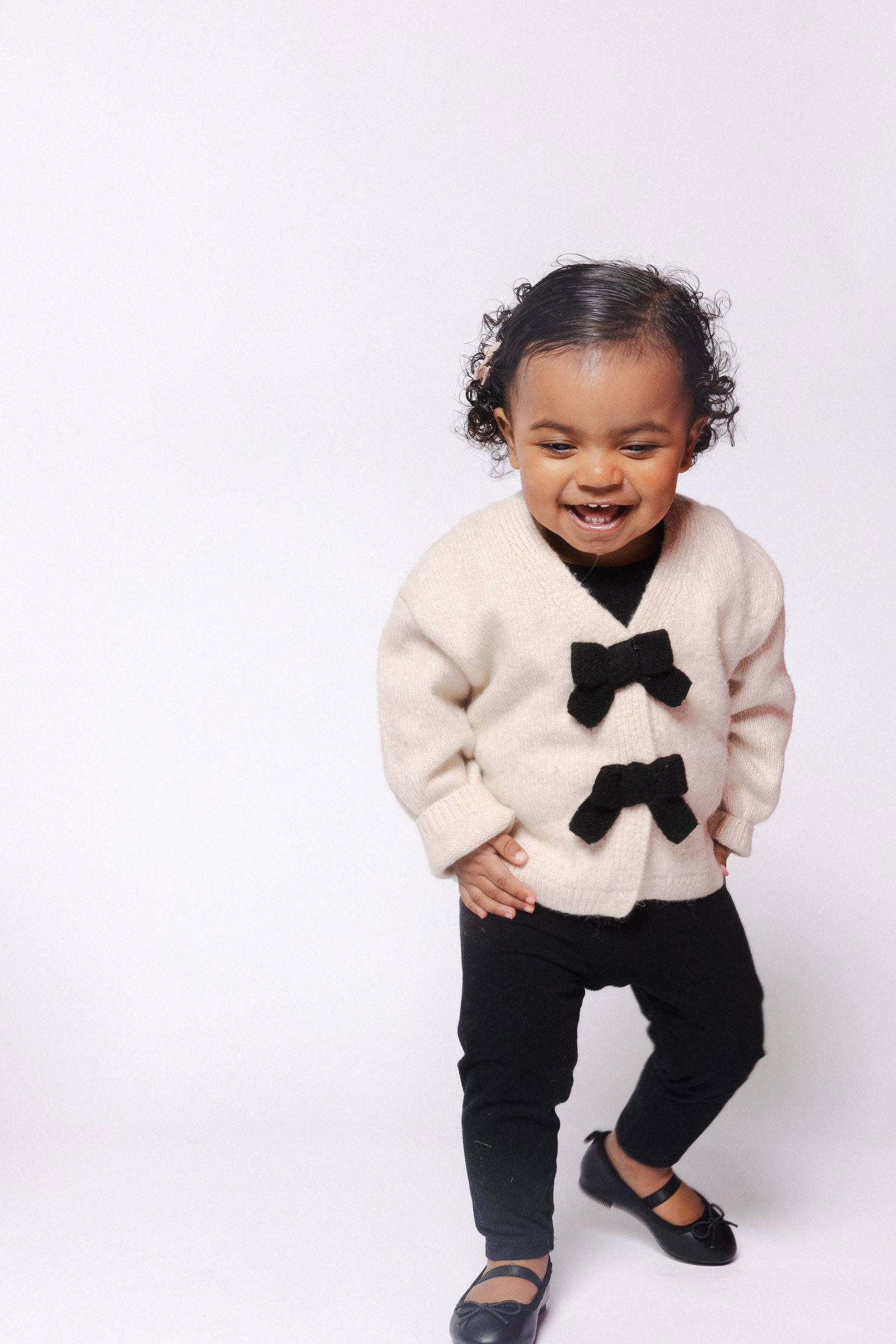 Toddler in cream sweater with black bow tie smiling and playing in various candid shots.