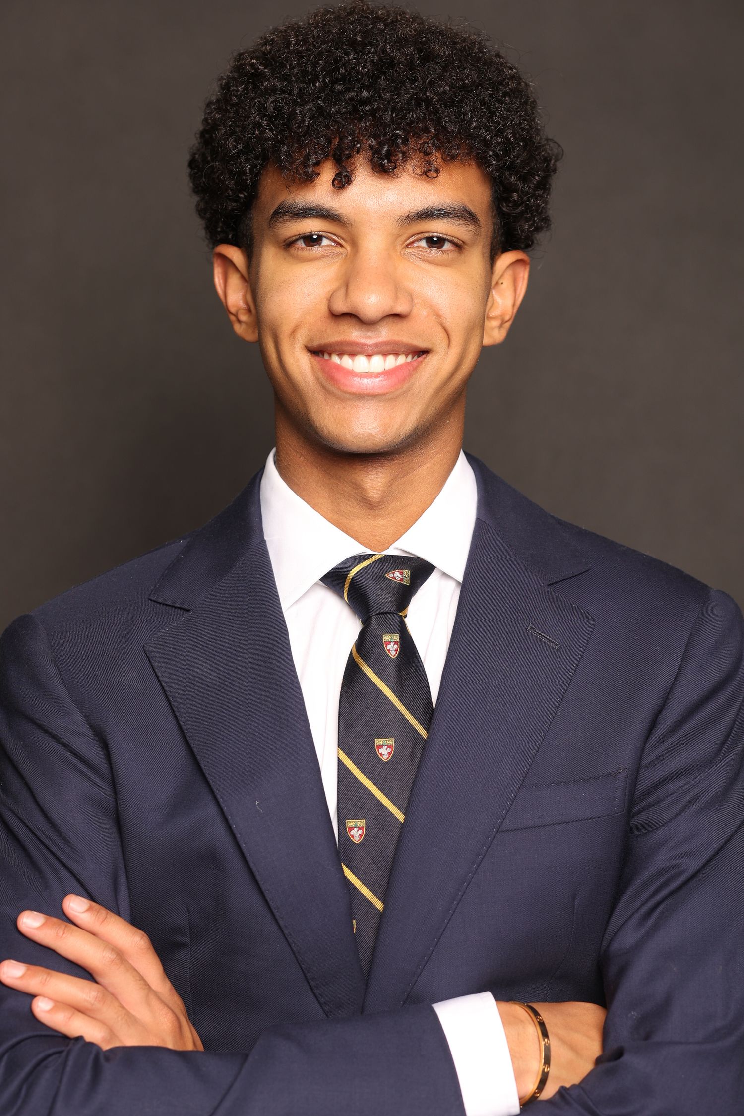 Young man in navy suit and striped tie posing professionally against dark background.