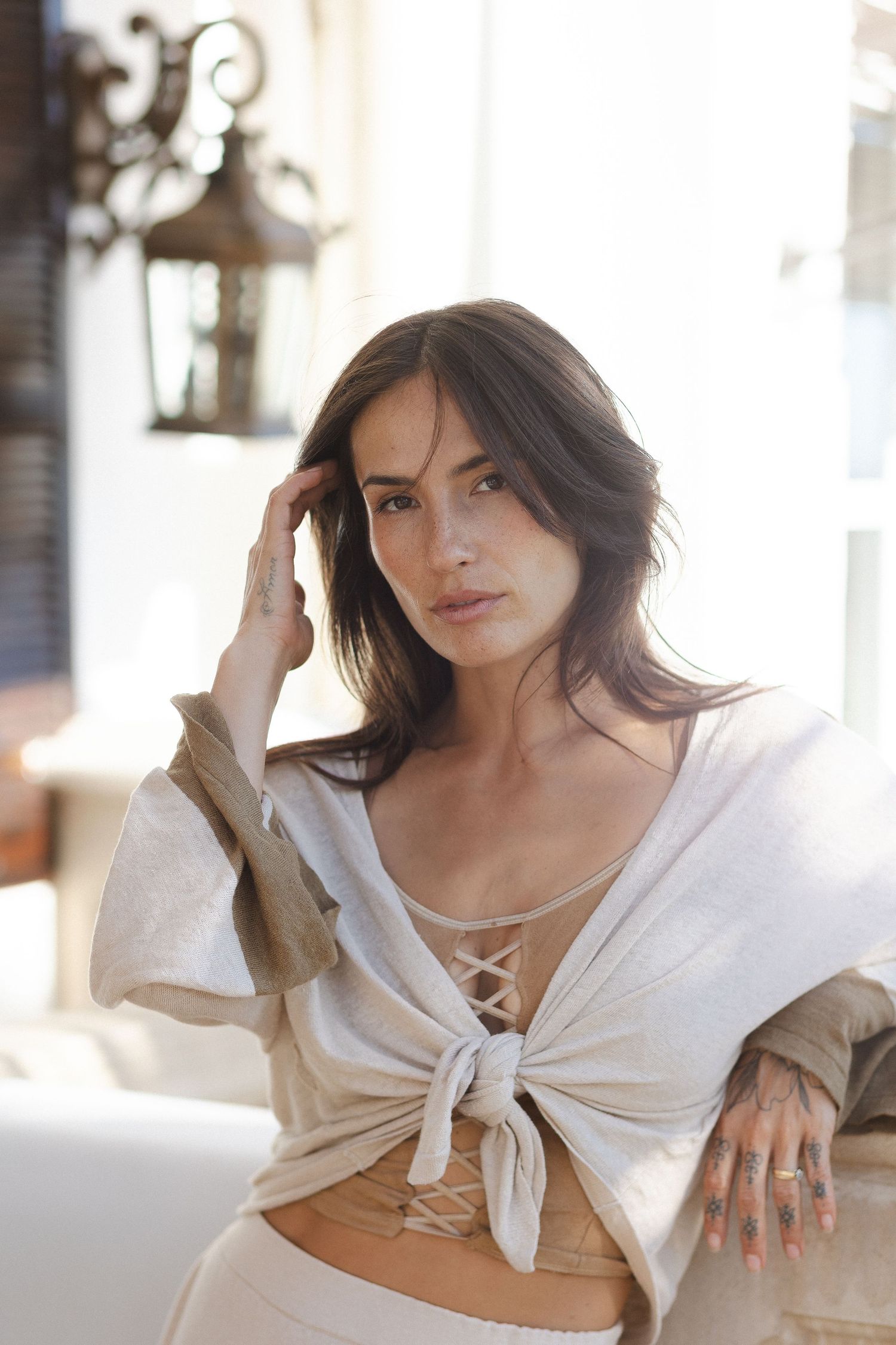 Model poses in casual white knotted top against bright interior background.