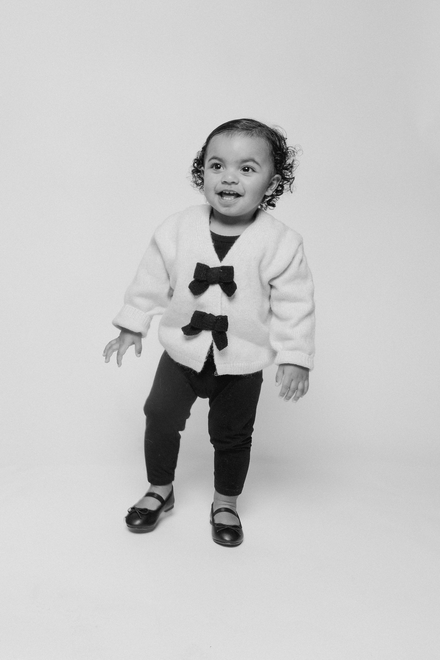 Small child wearing a formal white sweater with black bow tie and dark pants in multiple playful poses.