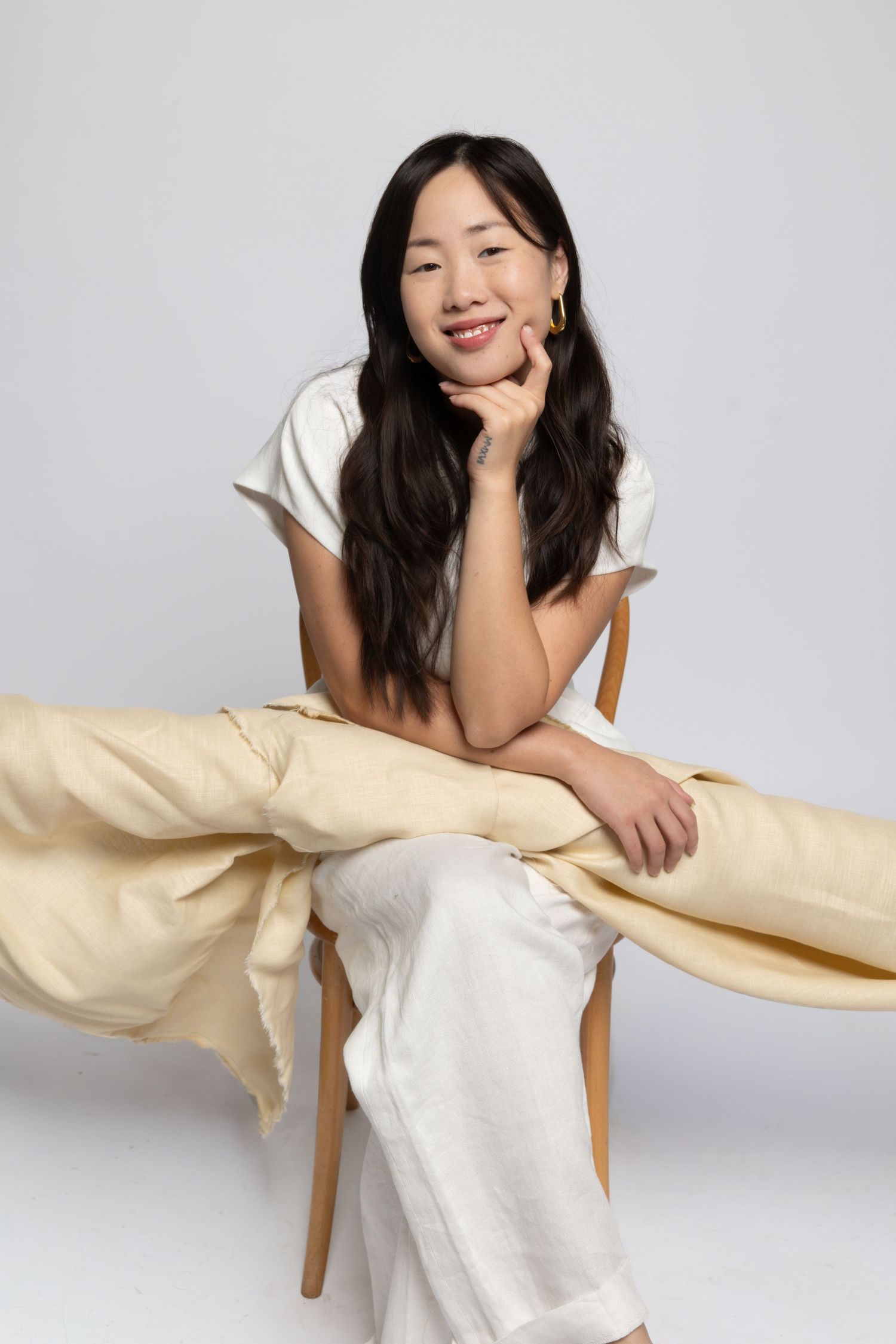 Woman in white top lounging with beige fabric in artistic studio portraits.