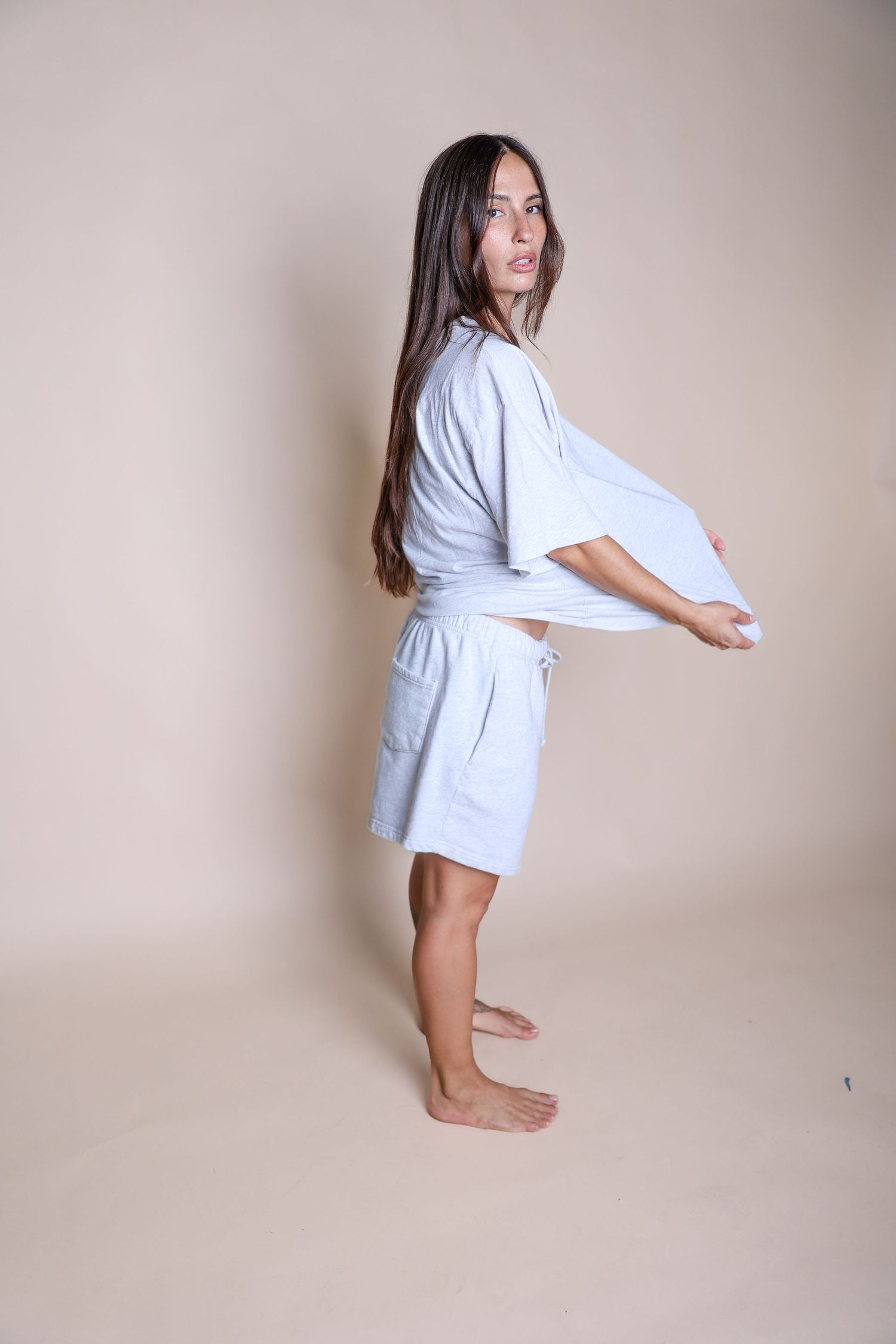 A person in white loungewear poses sideways against a neutral backdrop.