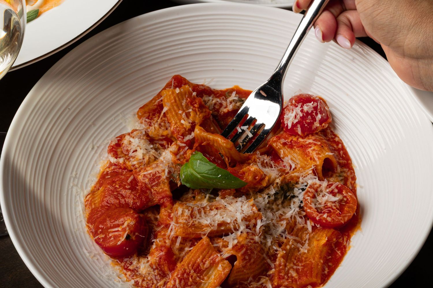 Red sauce pasta dishes garnished with herbs and cheese on white plates.