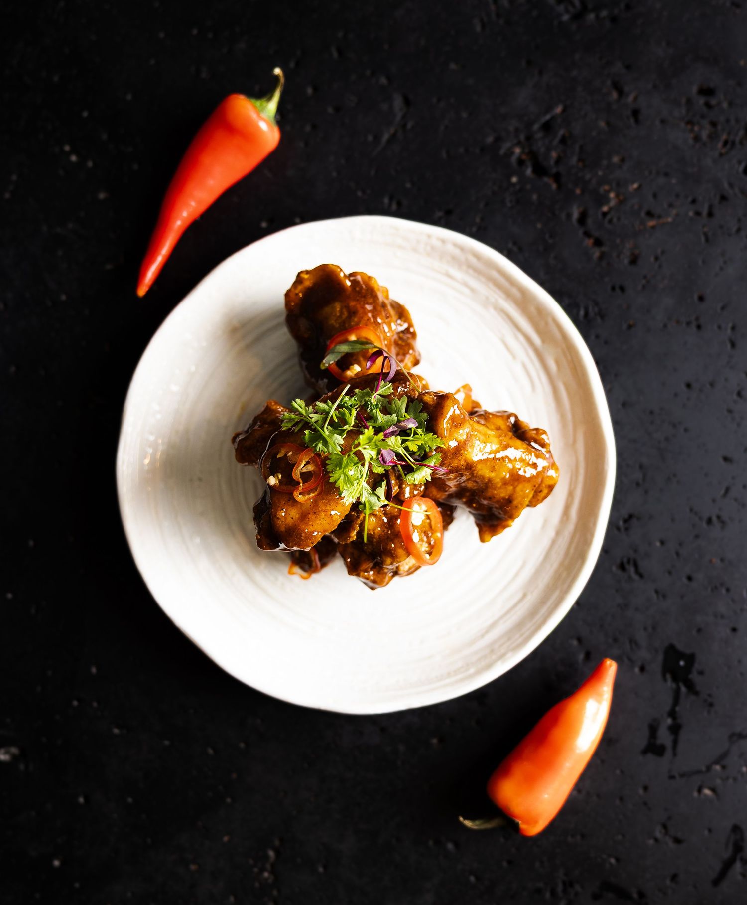 Crispy chicken wings garnished with herbs on white plates against dark background.