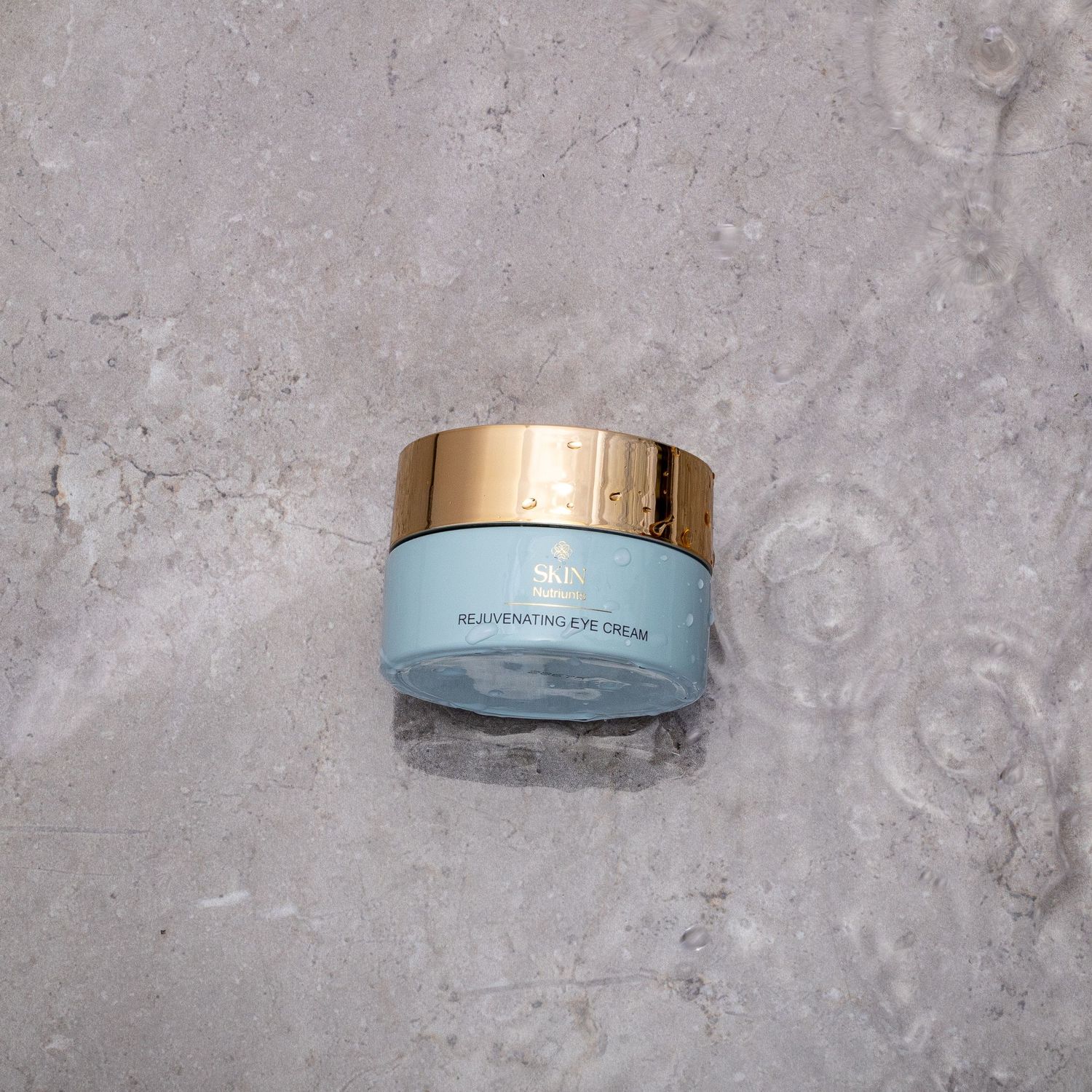 Luxury skincare cream jar with metallic gold lid photographed on gray stone background.