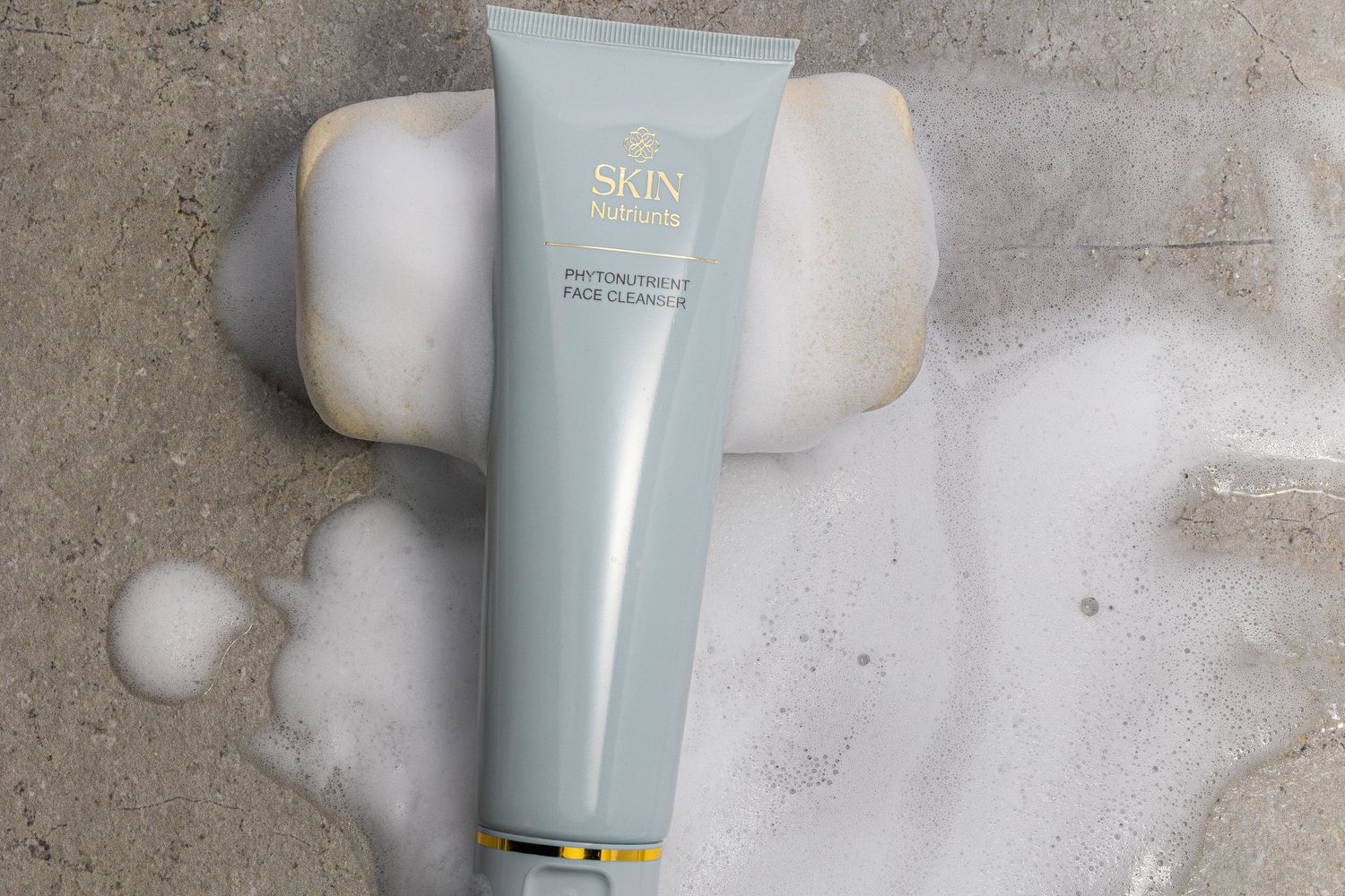 Luxury skincare face cleanser tube with foam bubbles against a textured concrete background.