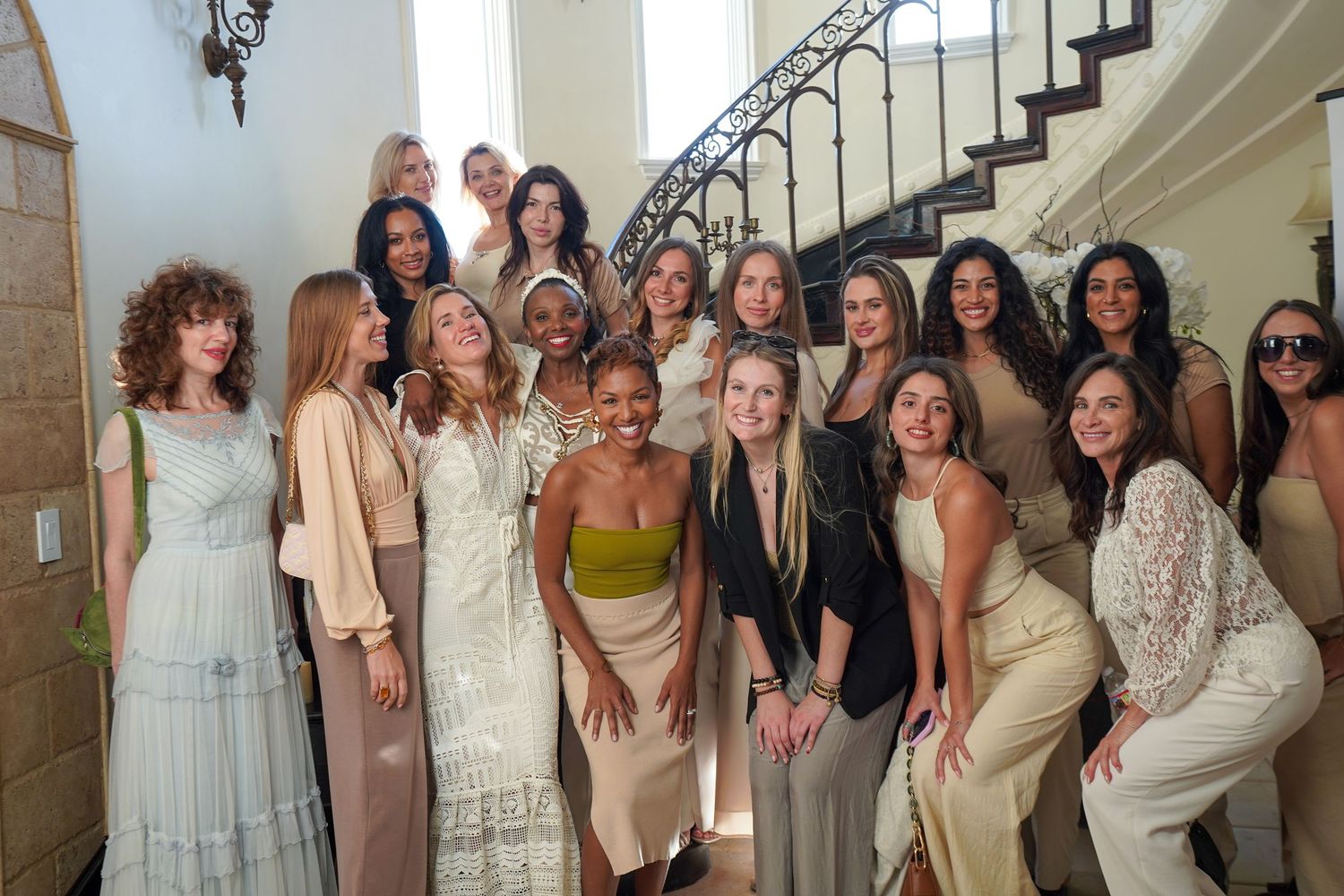 Group photo of people wearing coordinated neutral-toned dresses on a staircase.