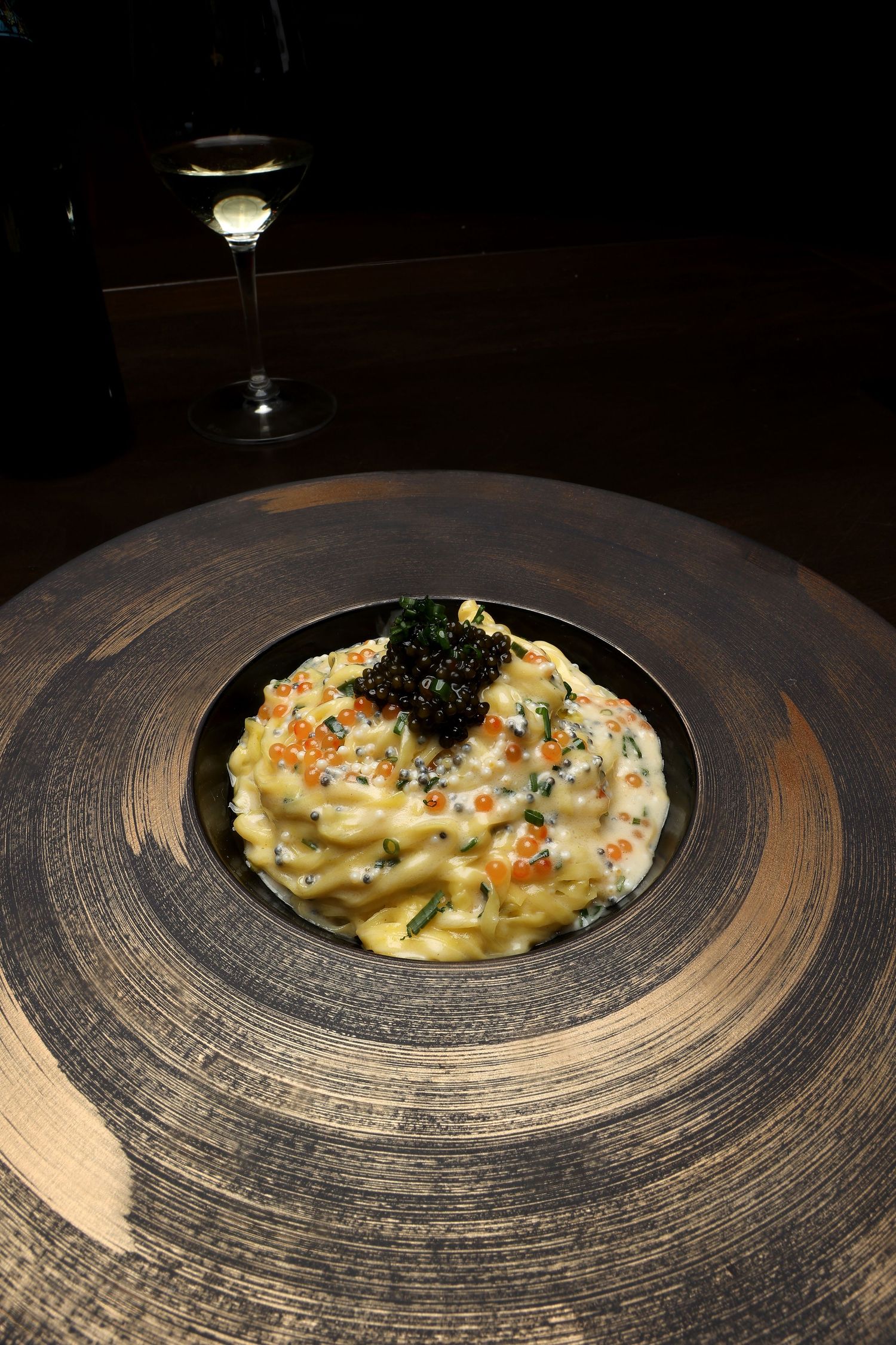 Creamy pasta dish with black garnish served in a modern circular plating design.