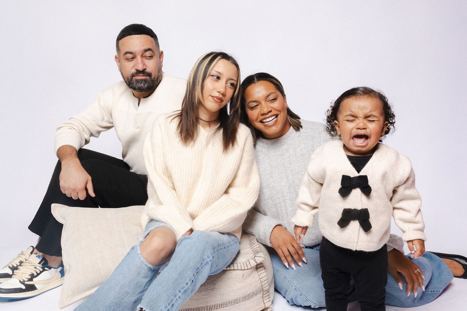 Family wearing coordinated cream and neutral outfits posing together on white background.