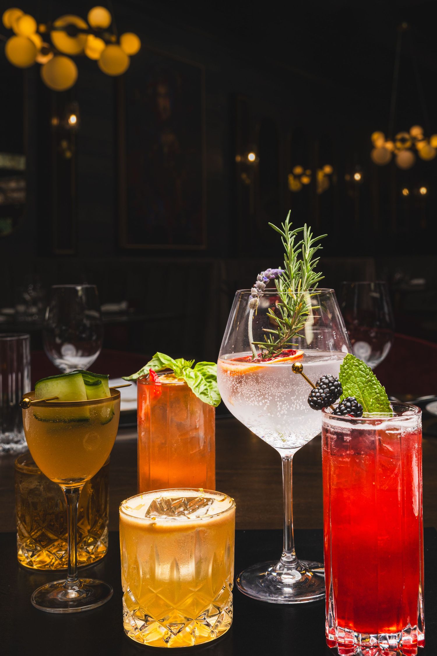 Artisanal cocktails with fresh garnishes and colorful ingredients displayed on a dark bar counter.