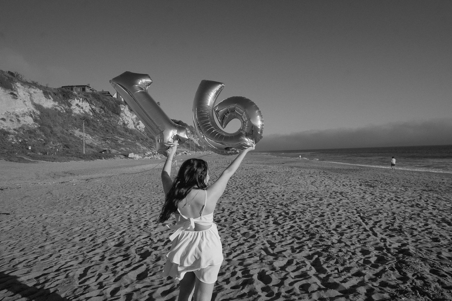 A person in white holds up a balloon number on a beach at sunset.