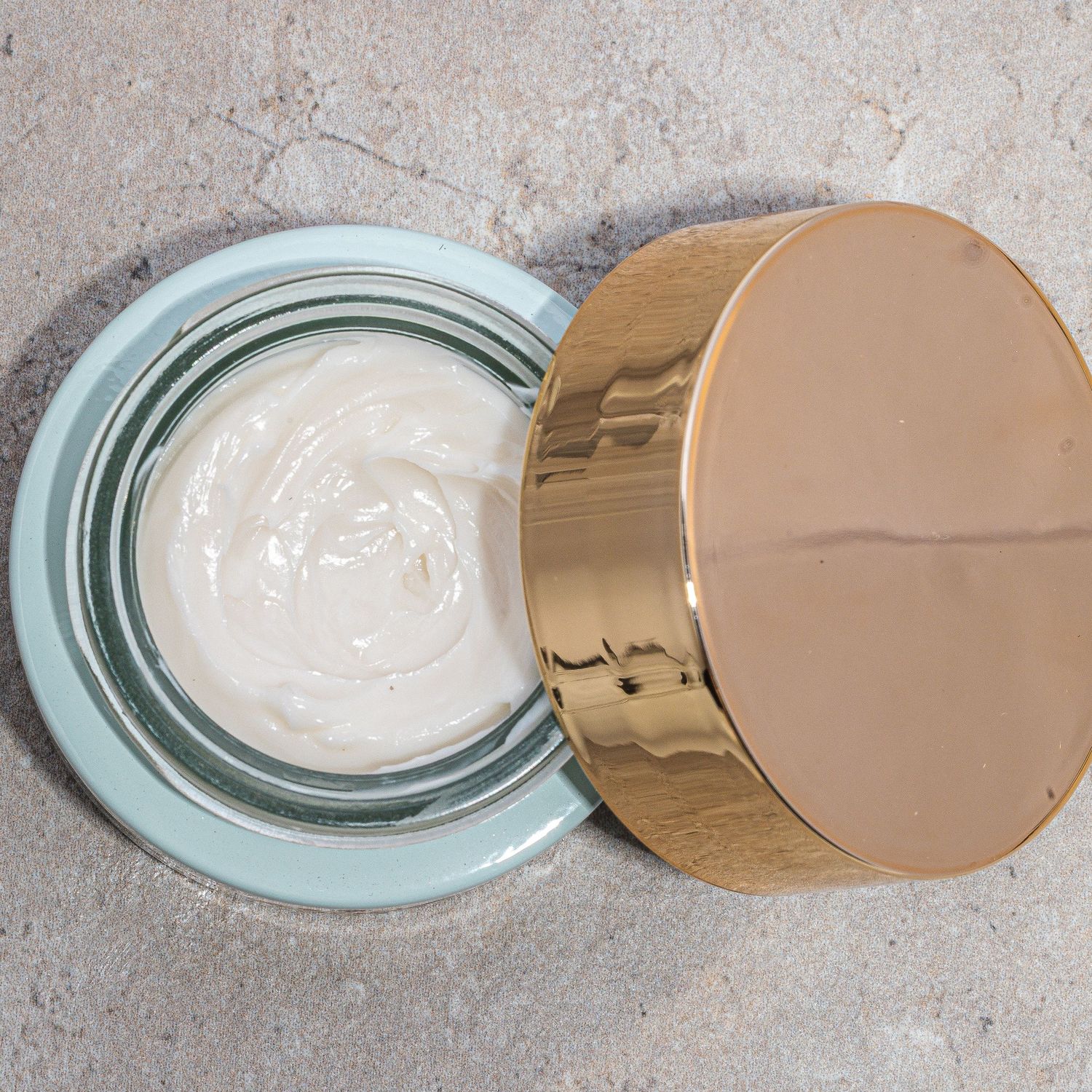 Open luxury cream jar showing white moisturizer texture with gold lid.