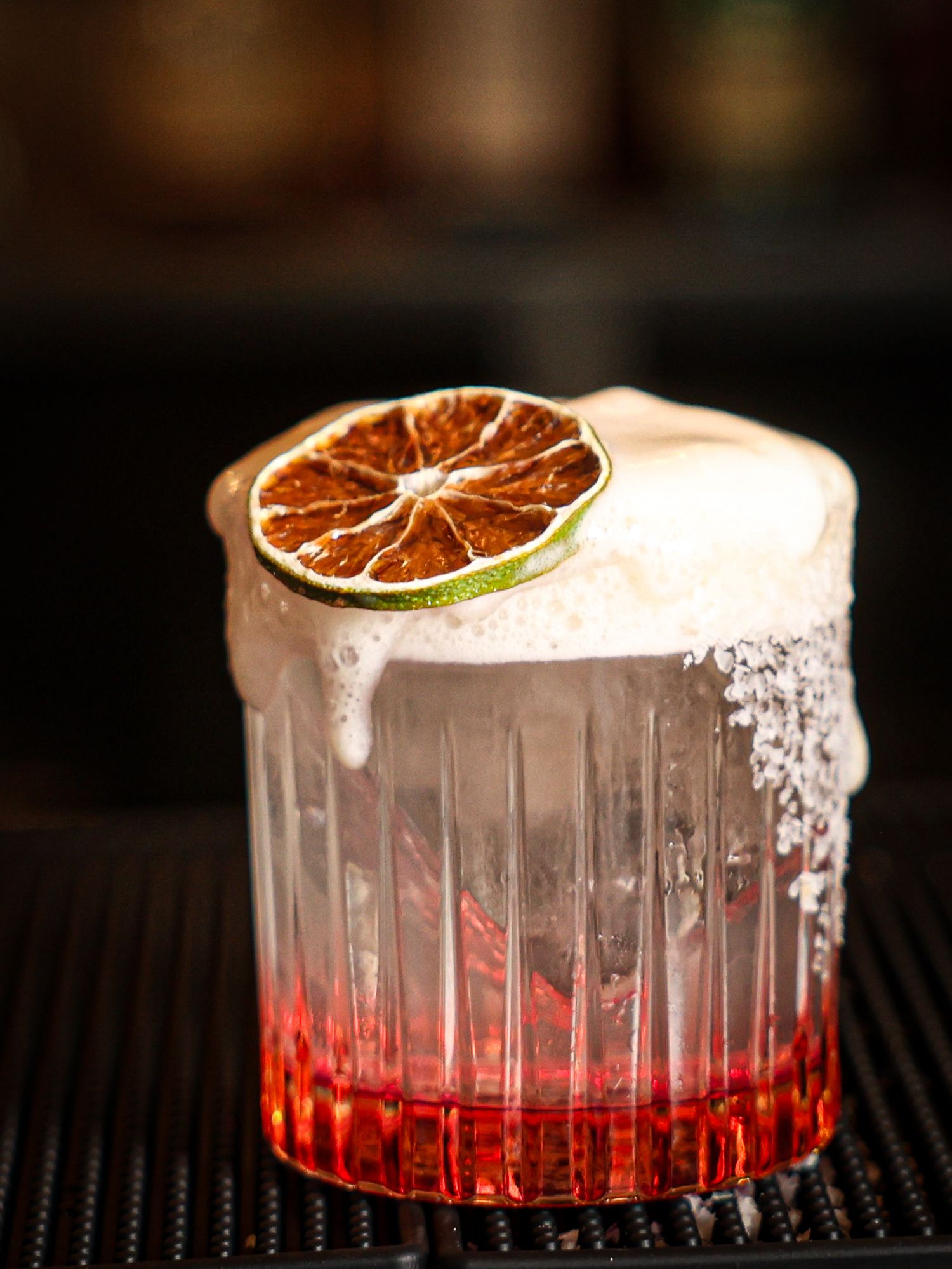 Red cocktail with dried citrus garnish and sugar rim in elegant glass.