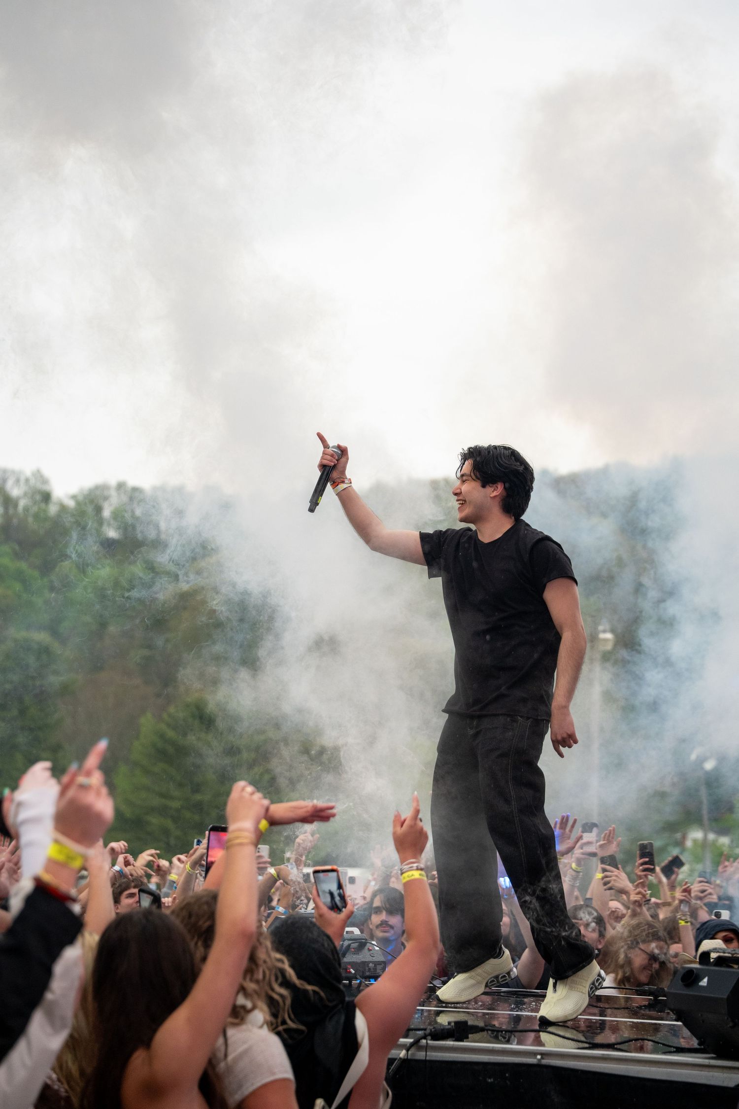 A male artist performs on an elevated platform surrounded by smoke at an outdoor festival.