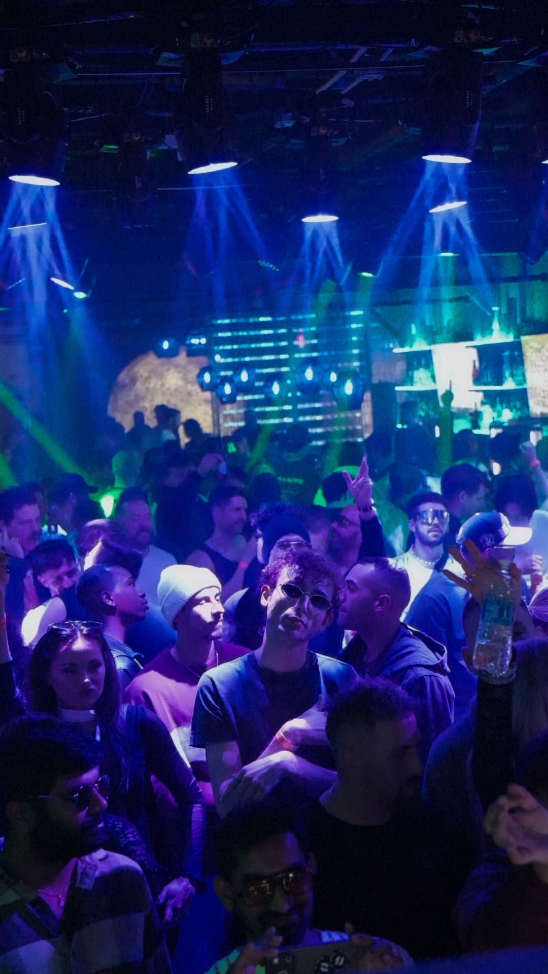 Large crowd dancing under colorful laser lights on a packed nightclub dance floor.