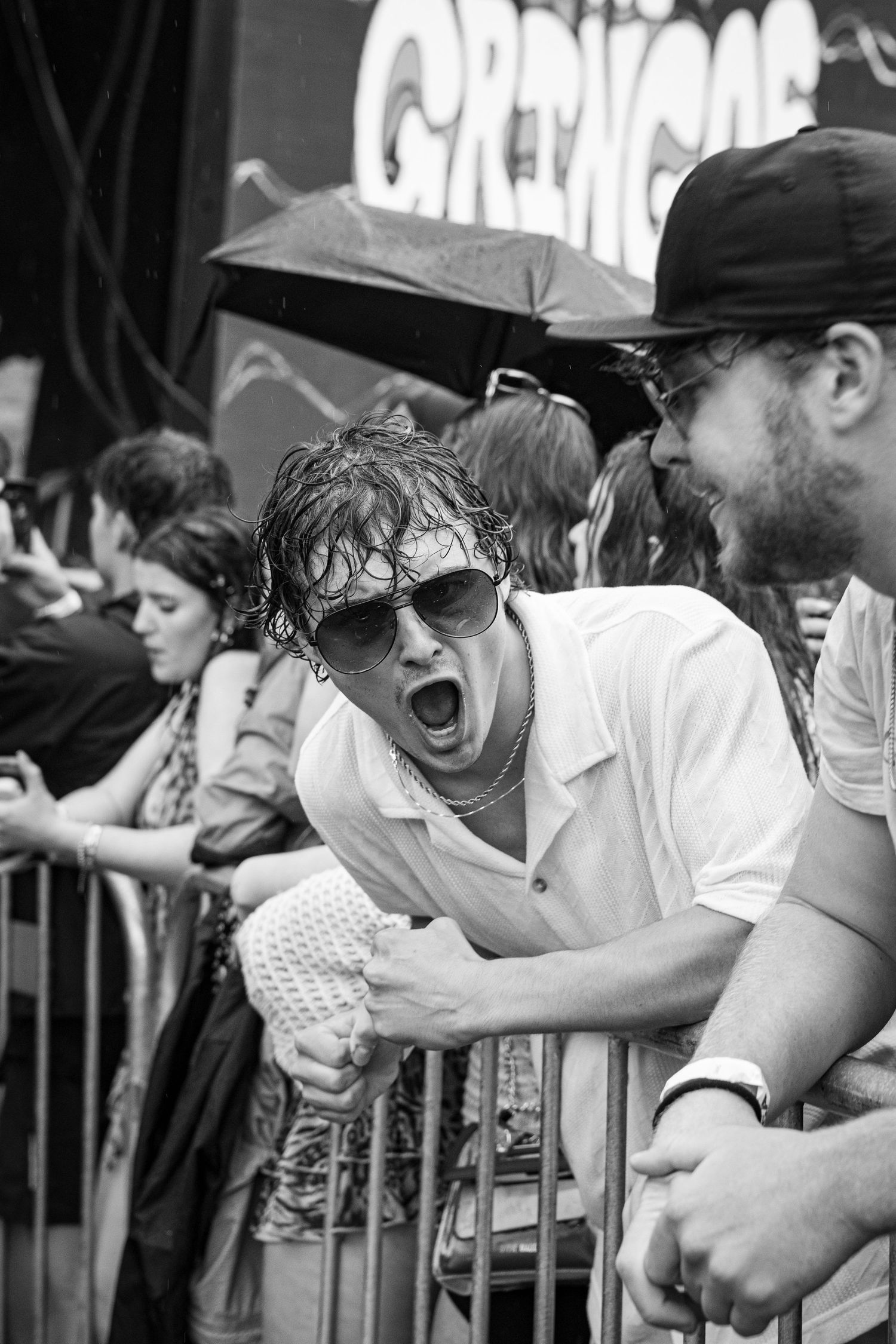 Black and white photo of enthusiastic wet festival fan yelling at barricade.