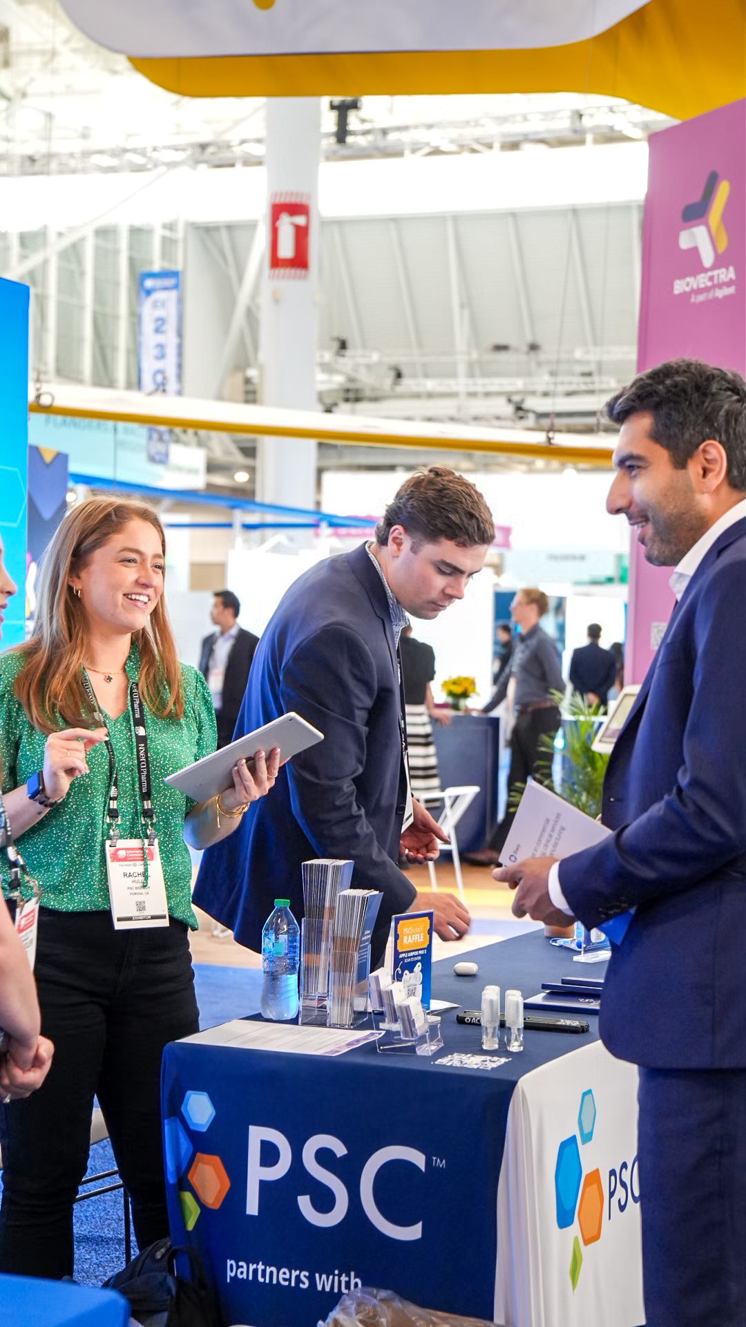 PSC company representative smiling at conference booth while engaging with attendees at trade show.