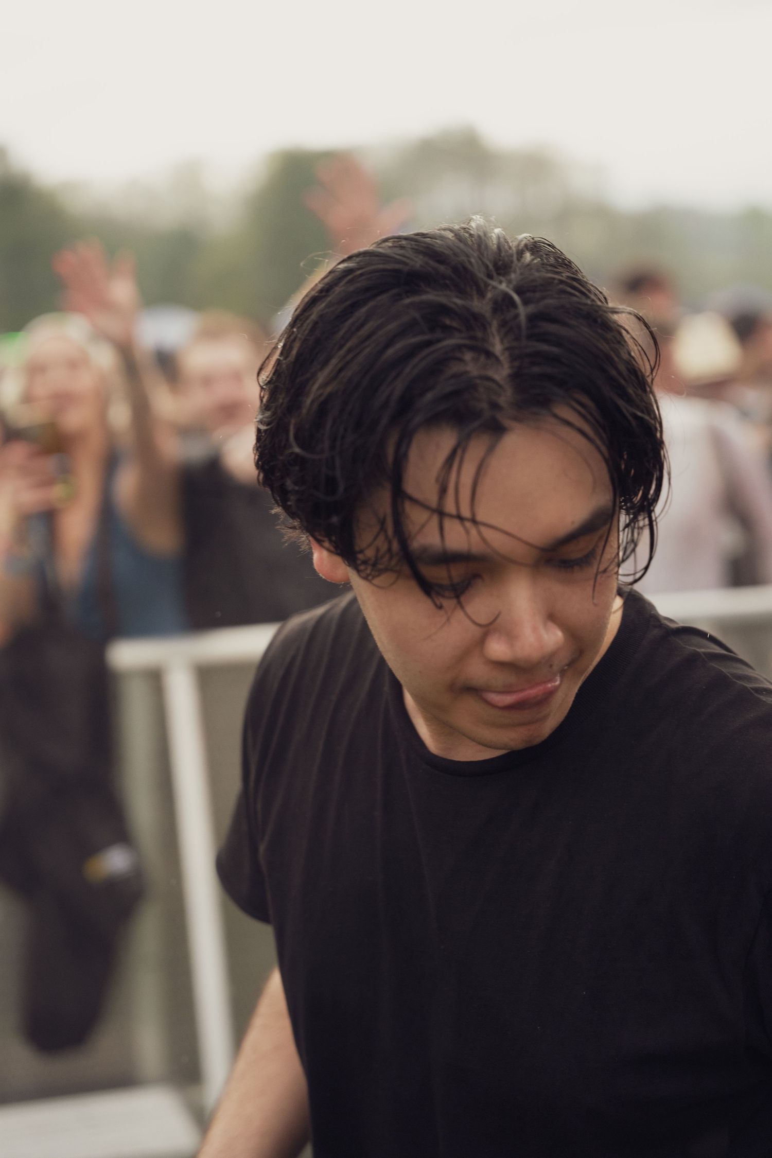 Young man with wet dark hair wearing black t-shirt at outdoor music festival.