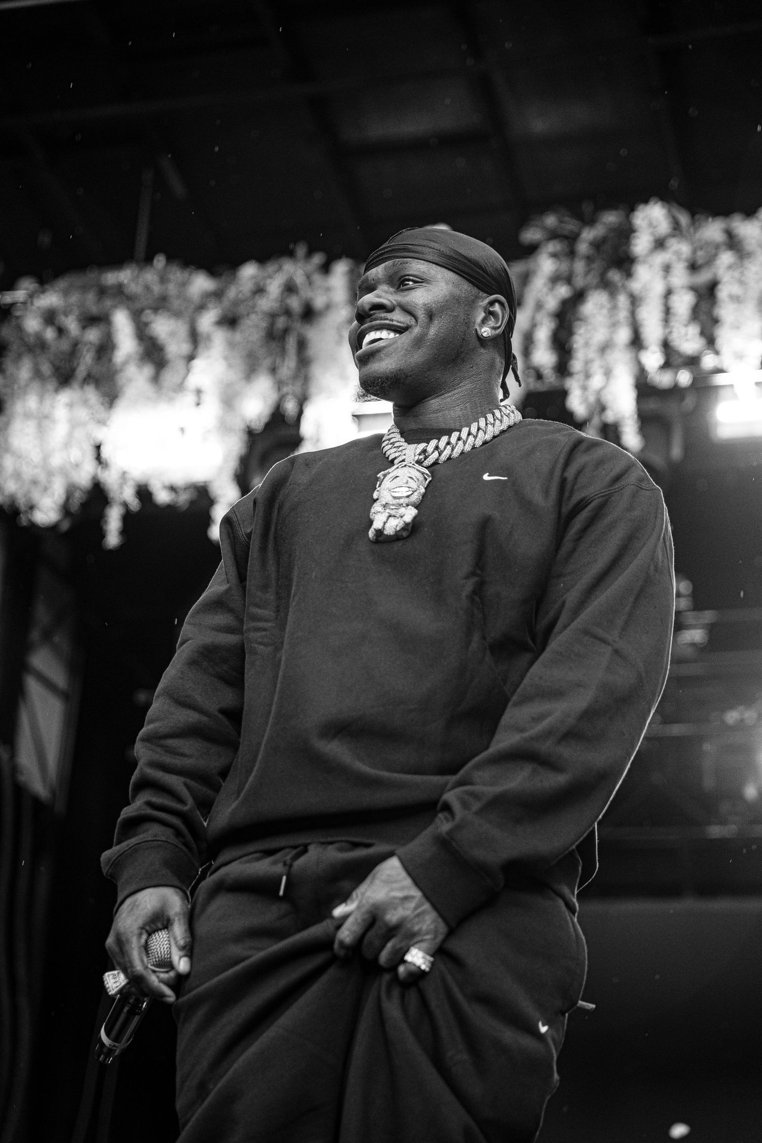 Black and white photo of a smiling male rapper performing on stage wearing a Nike sweatshirt and chain.