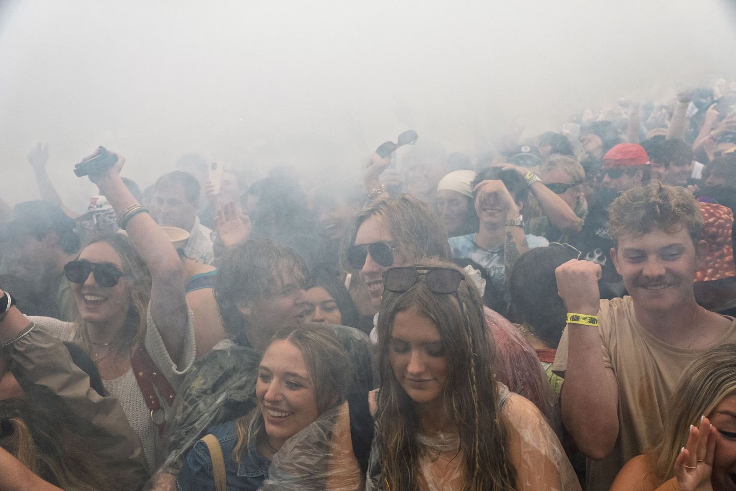 Large crowd of festival-goers dancing in fog or smoke at an outdoor music event.