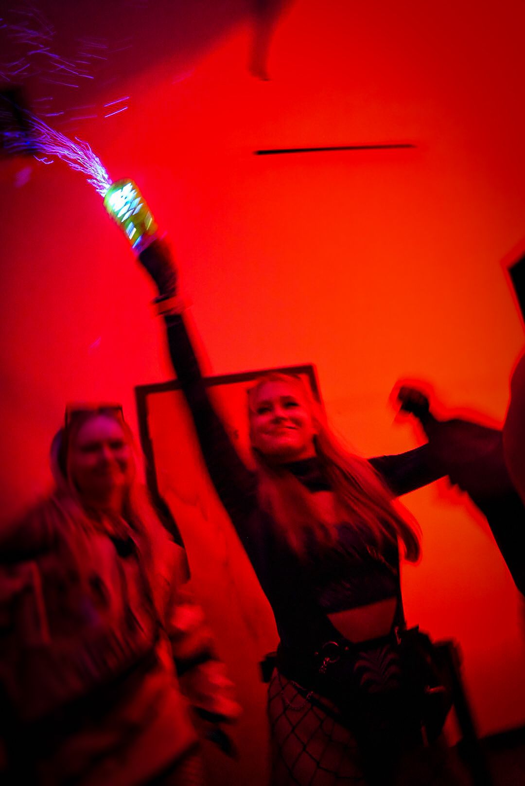Woman dancing joyfully while holding a glowing light wand at a red-lit party.
