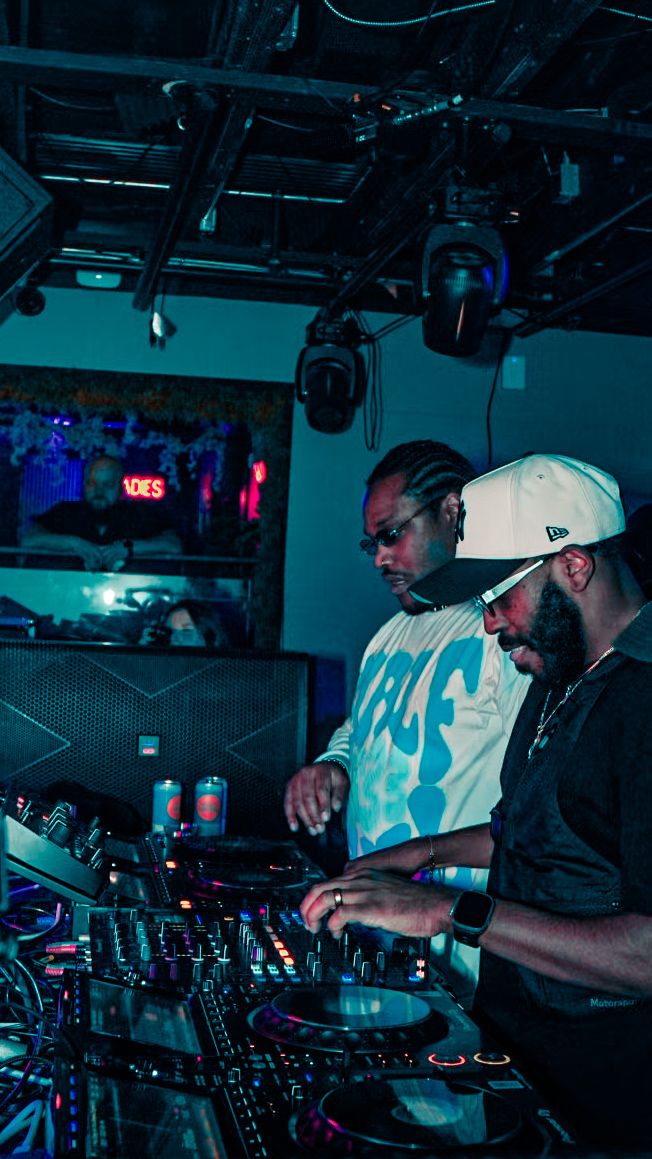 Two DJs mixing music on turntables under blue neon lights in a nightclub.