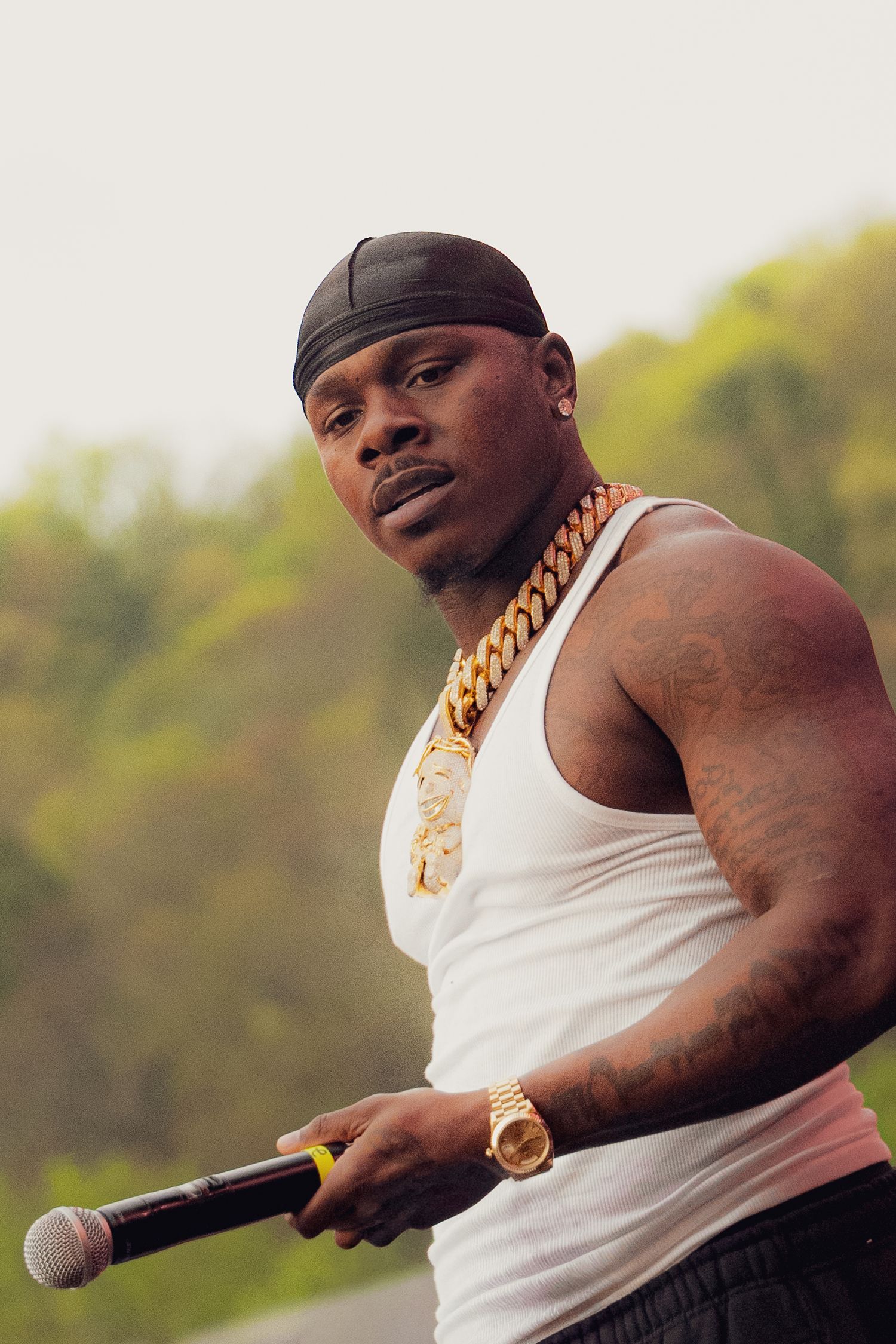 Close-up portrait of rapper holding microphone wearing gold chain and white tank top.