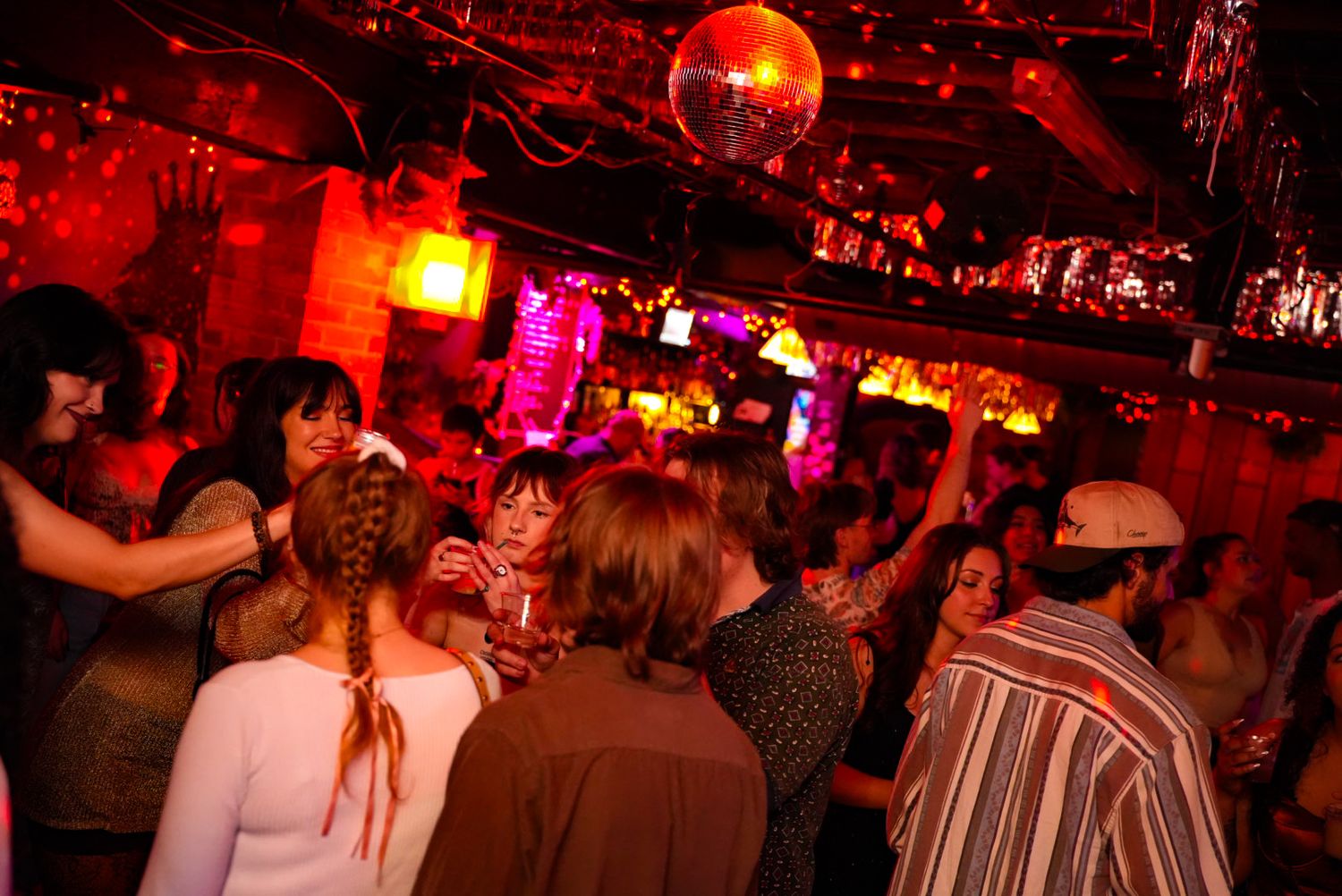 Crowded nightclub with red lighting, disco ball, and people dancing and socializing at a lively bar event.