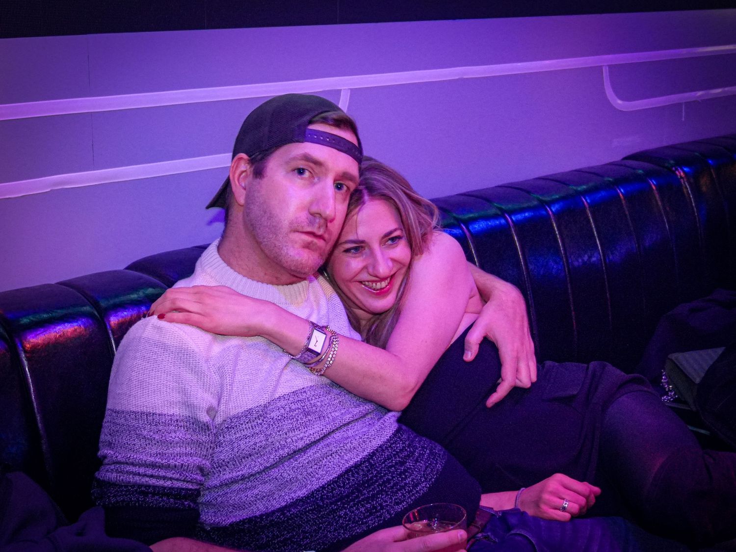Couple relaxing together on a couch in a purple-lit nightclub VIP lounge area.