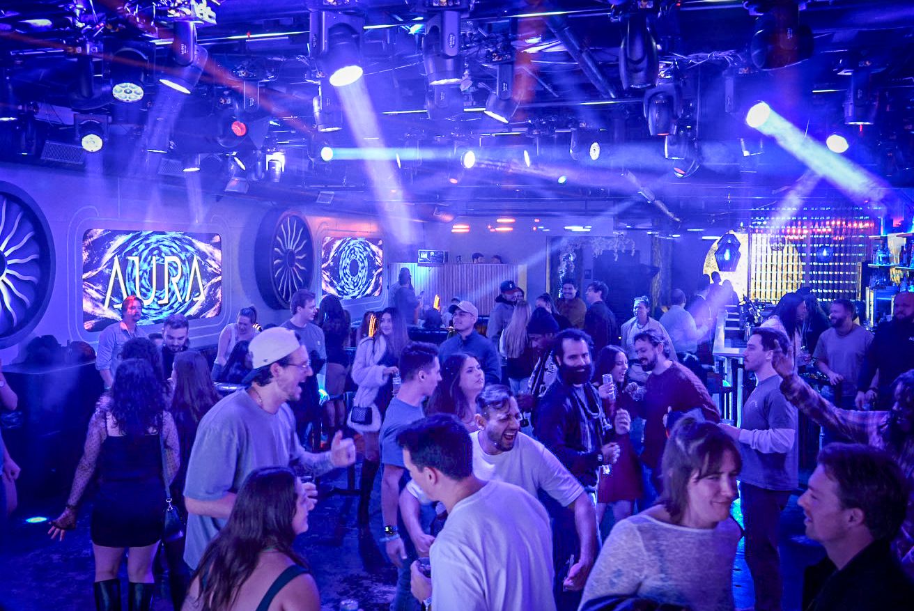 Crowd of people dancing at a nightclub with blue stage lights and LED screens displaying MARA logo.