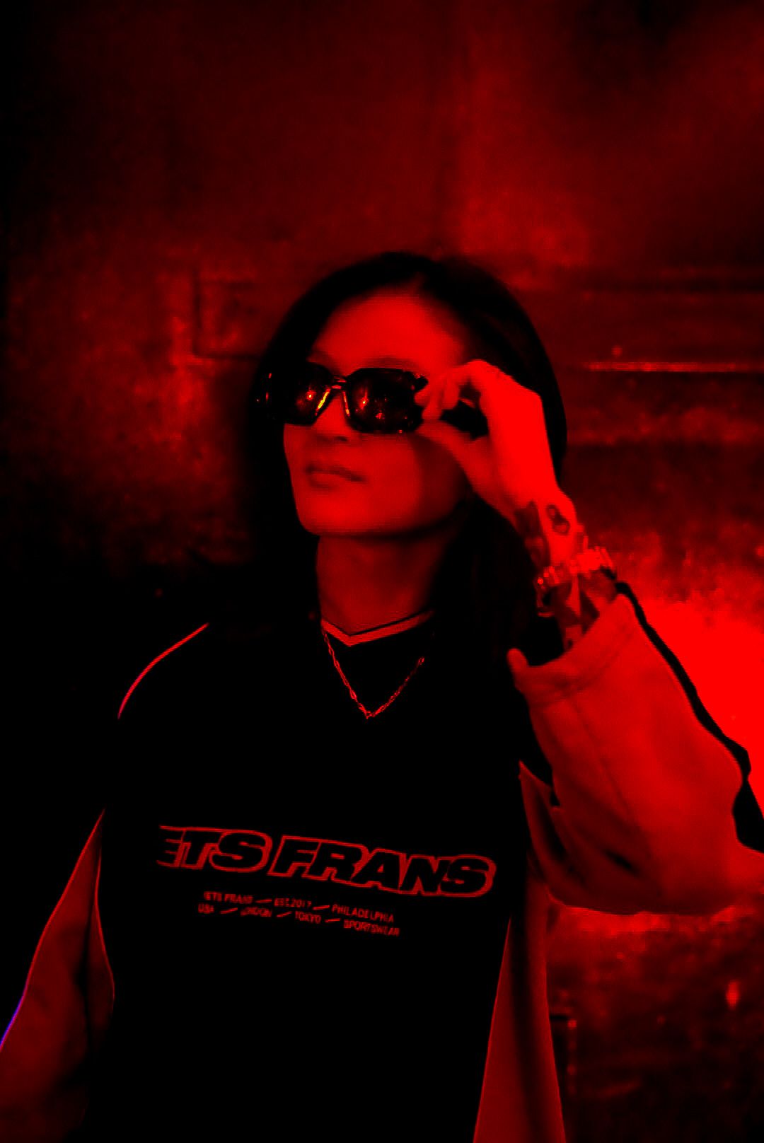 Woman in Jets Frans shirt adjusting sunglasses under dramatic red lighting.