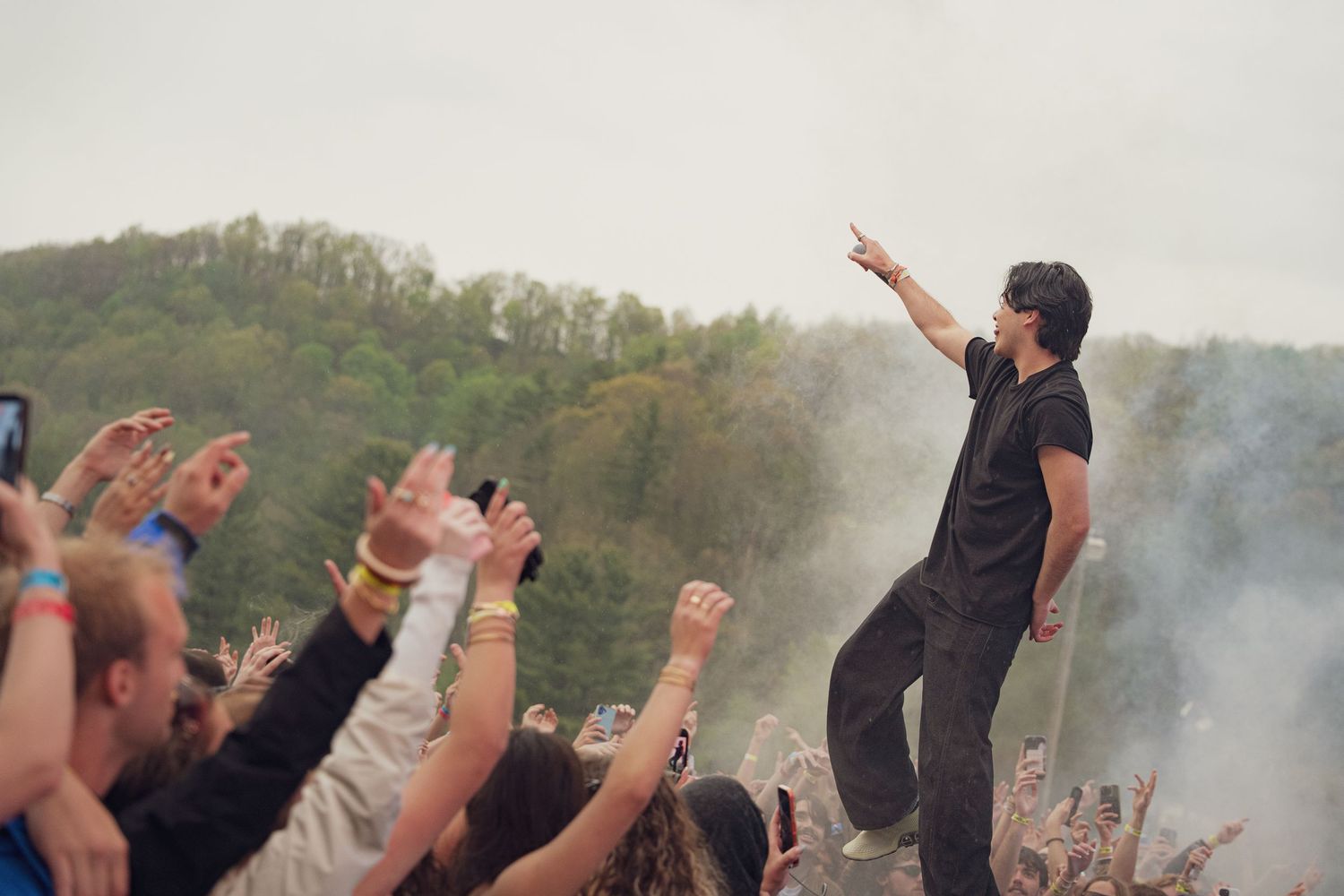 Artist pointing to crowd while standing elevated above fans at an outdoor music festival.