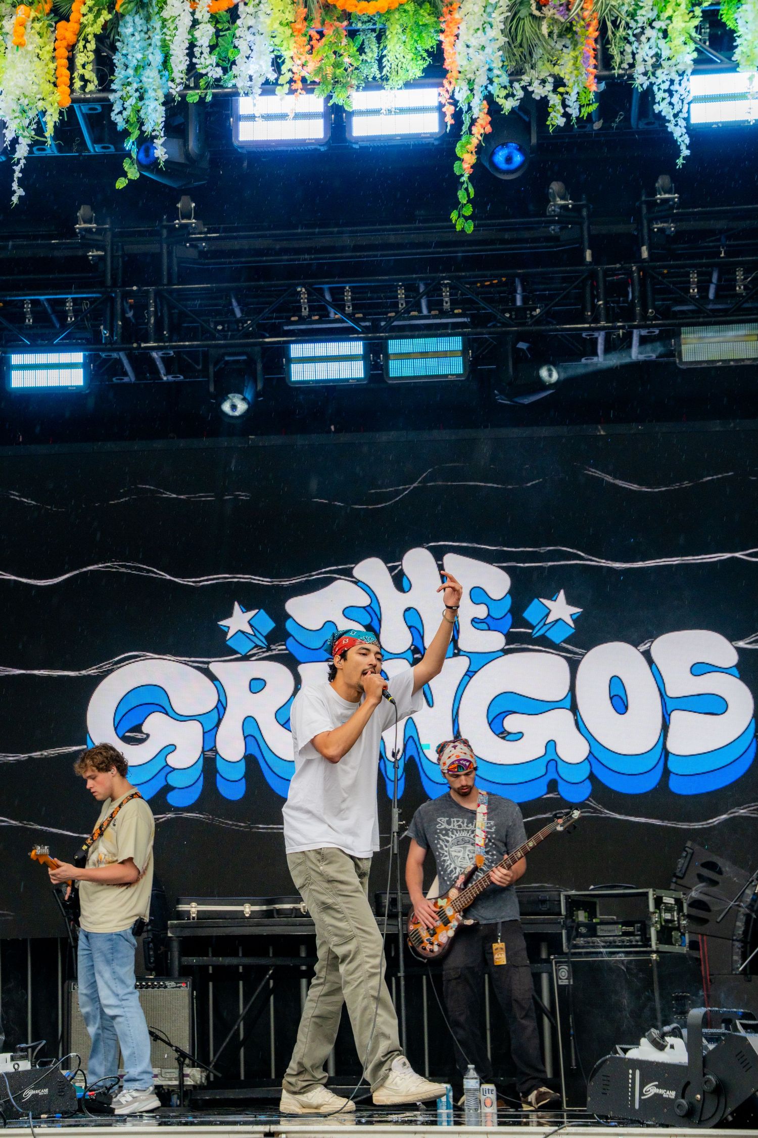 The Gringos band performing live on stage with floral backdrop and lights.