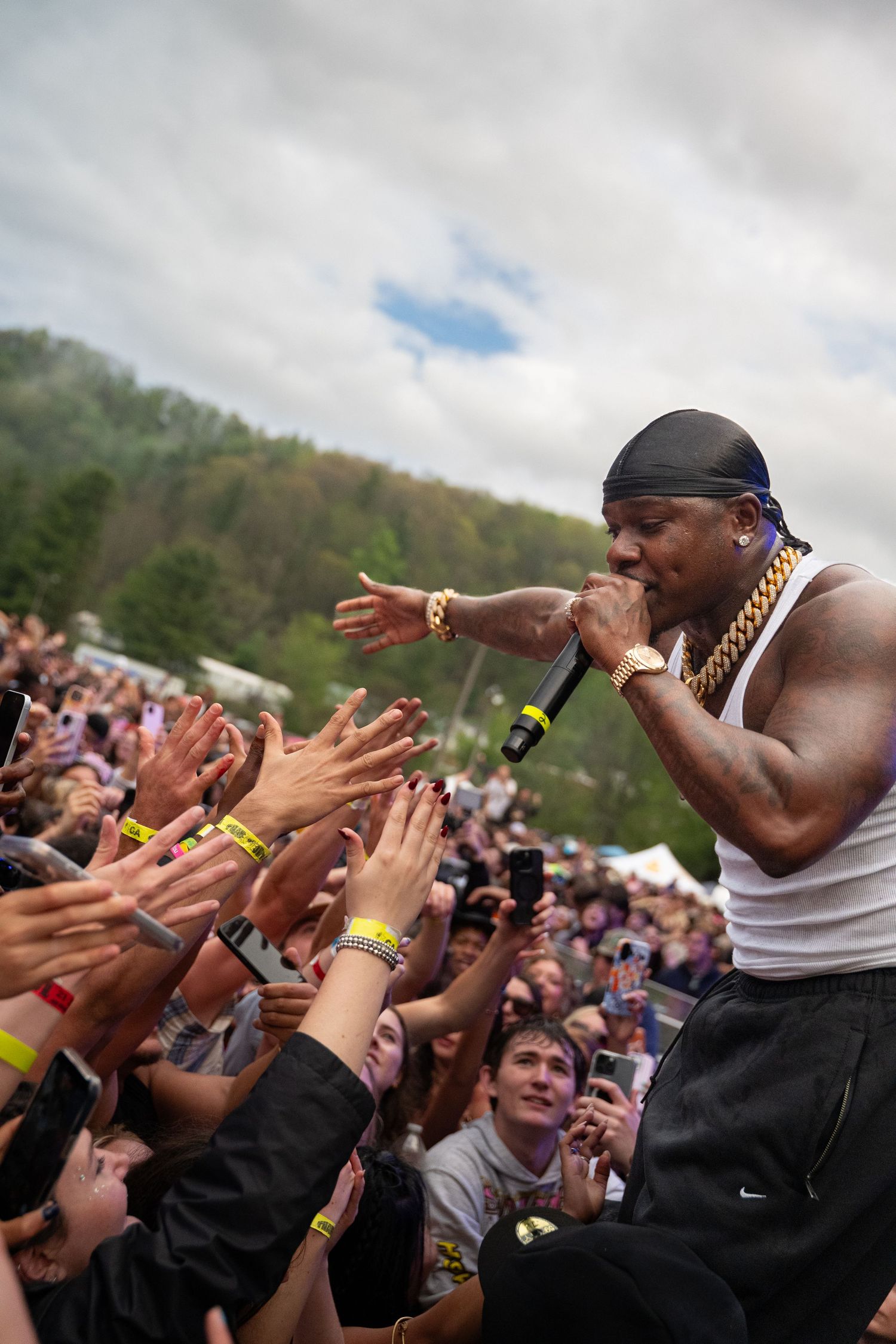 A muscular performer in a white tank top engages with fans at an outdoor music festival.