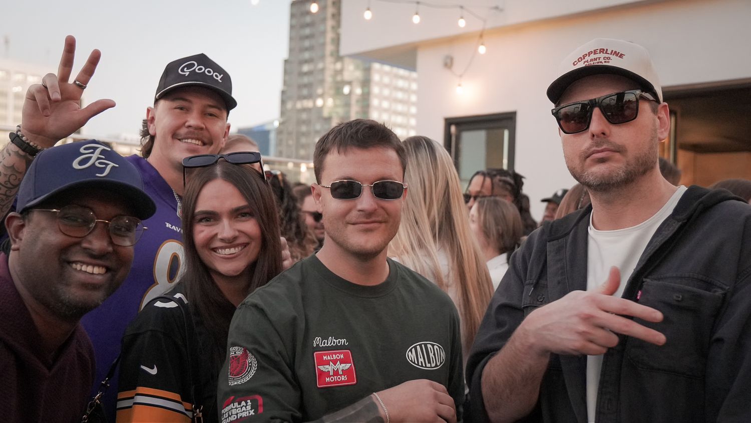 A group of friends smiling and posing together at an outdoor rooftop event.