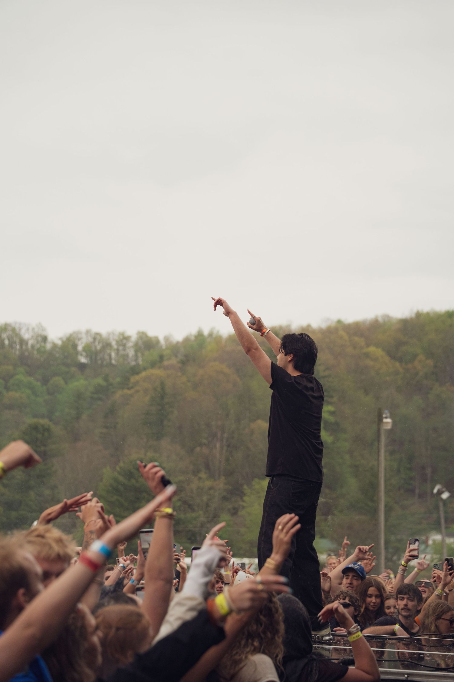 Man in black outfit crowd surfing with arms raised at outdoor music festival.