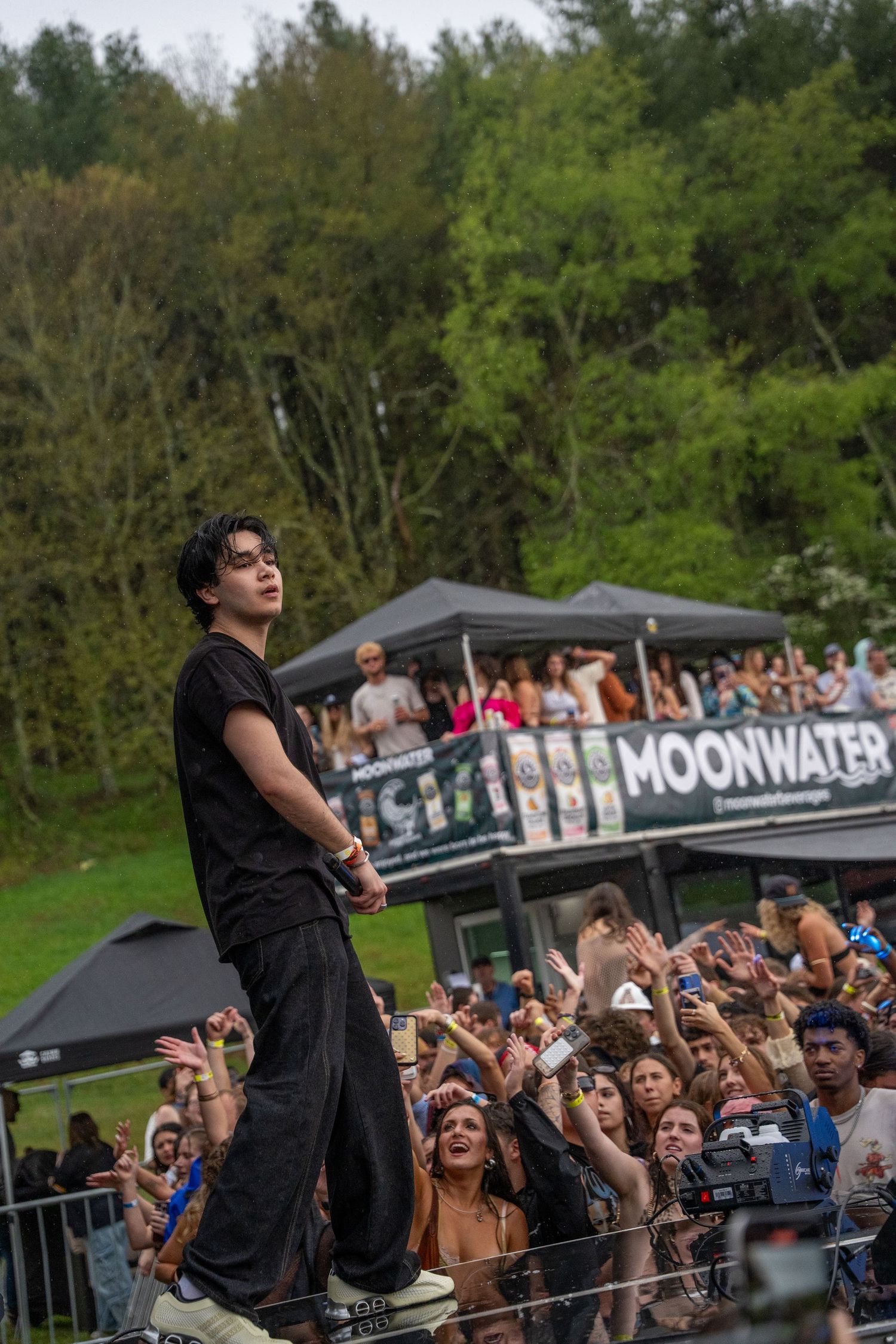 A performer in all black stands on stage before an enthusiastic crowd at a Moonwater festival.