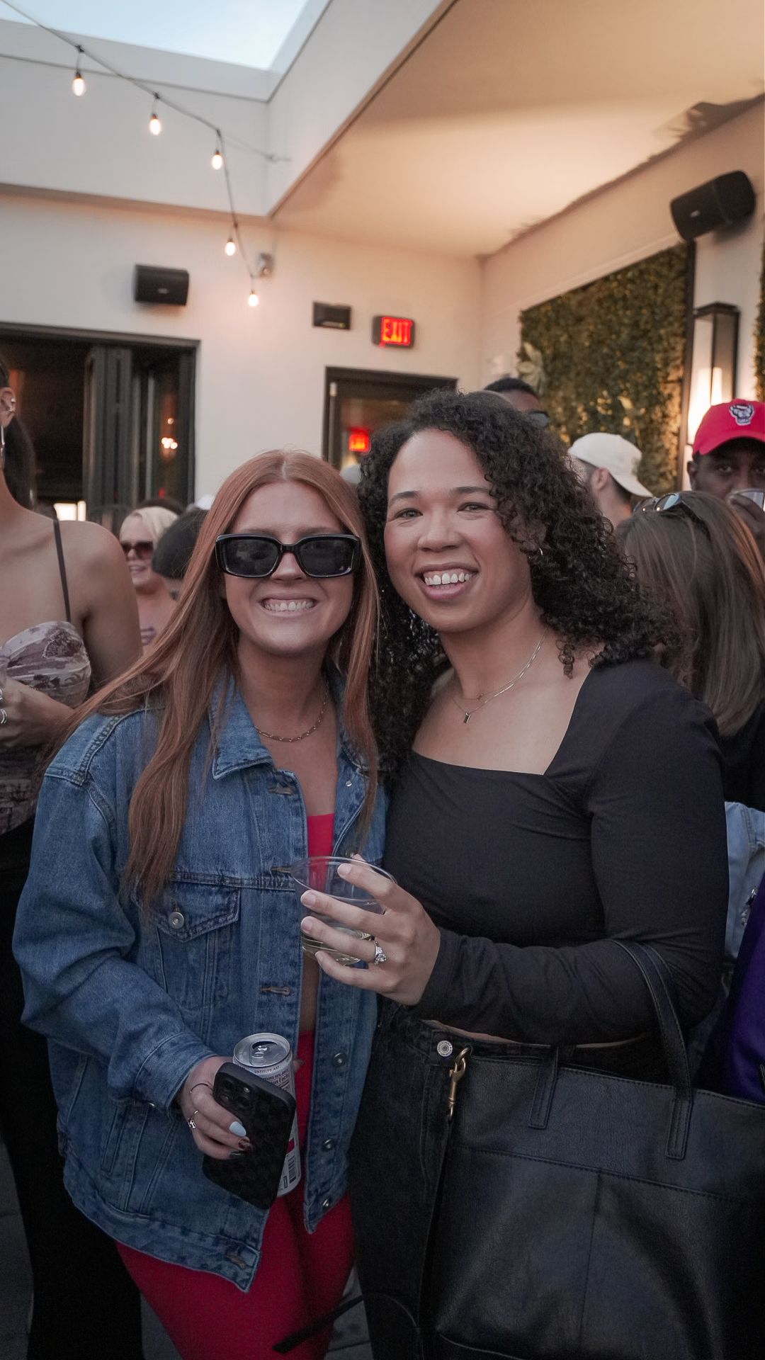 Two women smiling together at a lively outdoor evening party event.