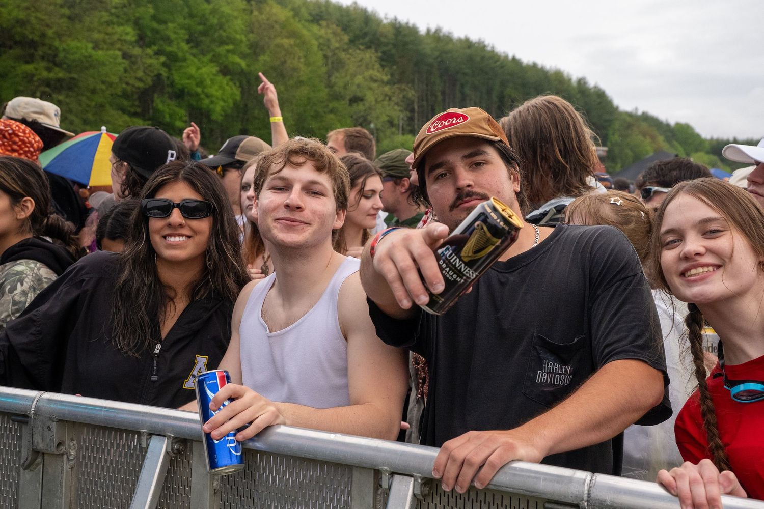Group of smiling young festival attendees posing at barrier fence at outdoor music event.