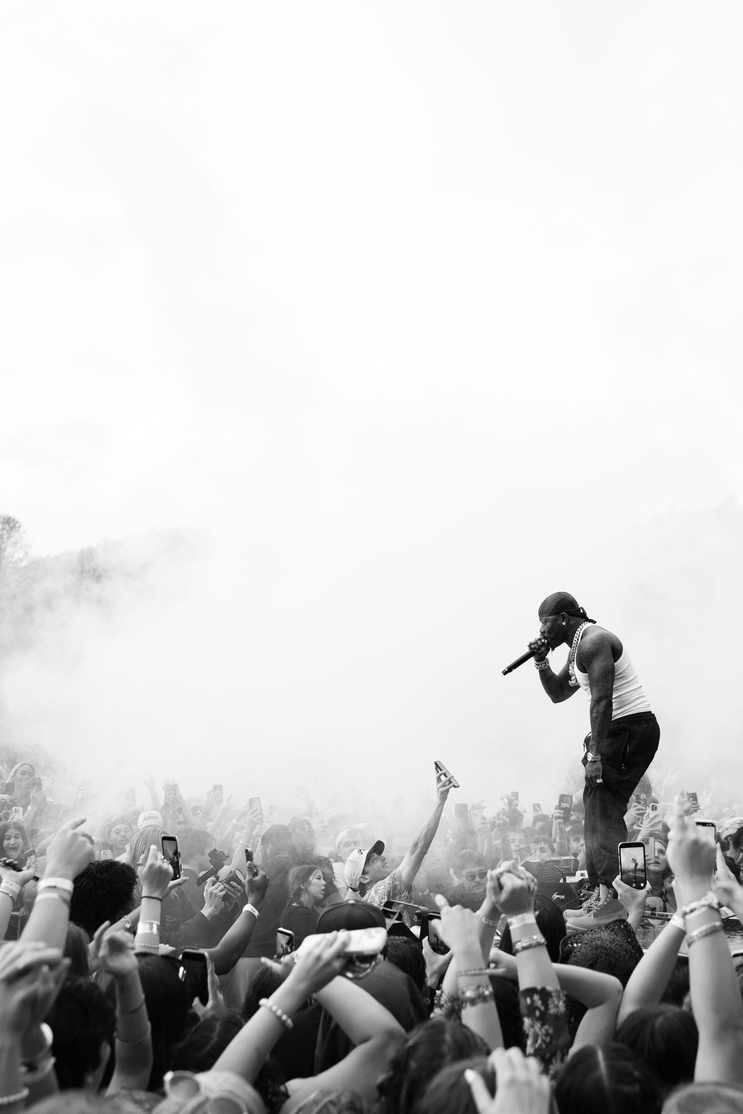 Black and white photo of rapper performing above smoky crowd at outdoor festival.
