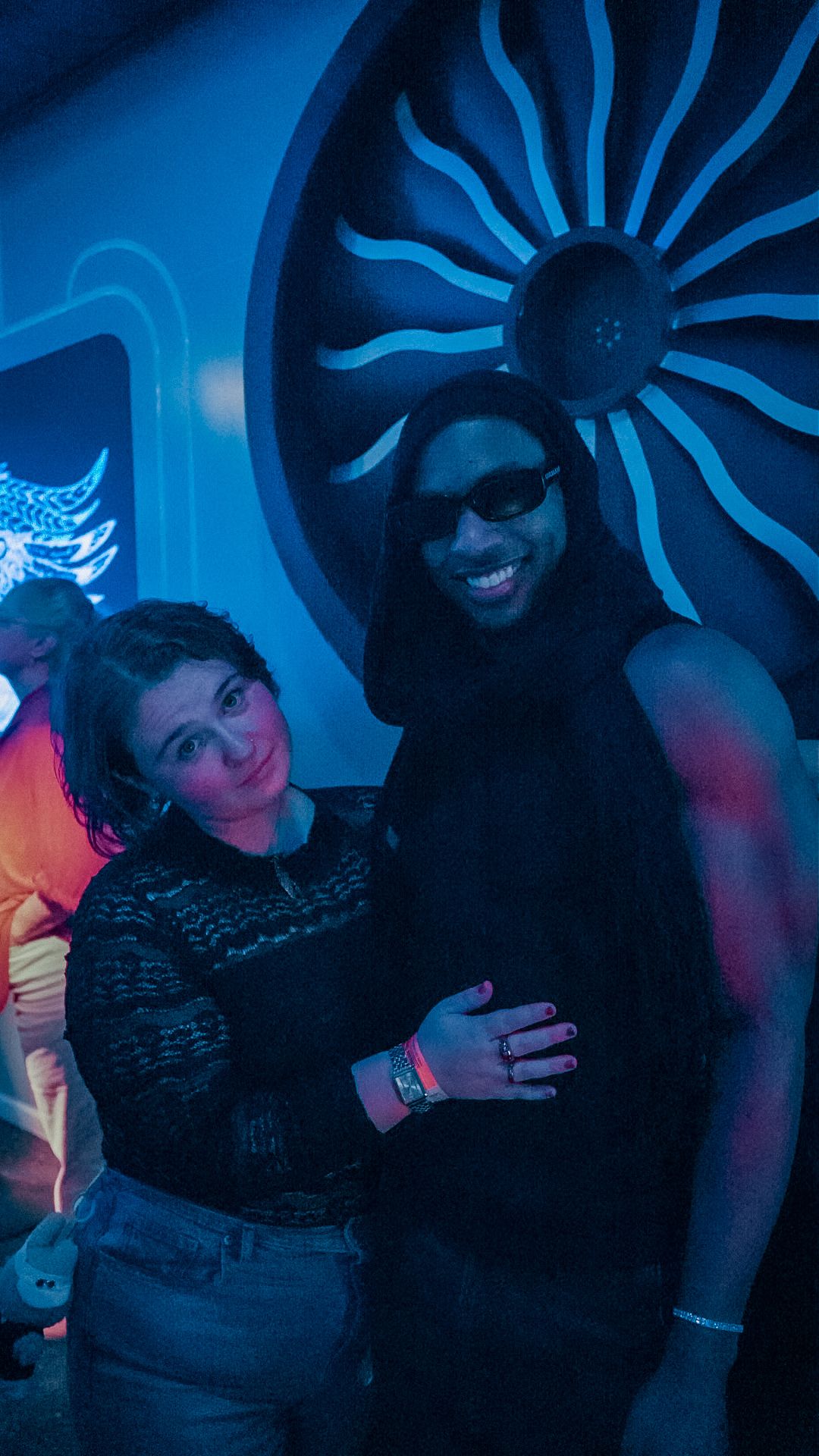 Couple smiling together in front of a glowing turbine art installation at a nightclub.