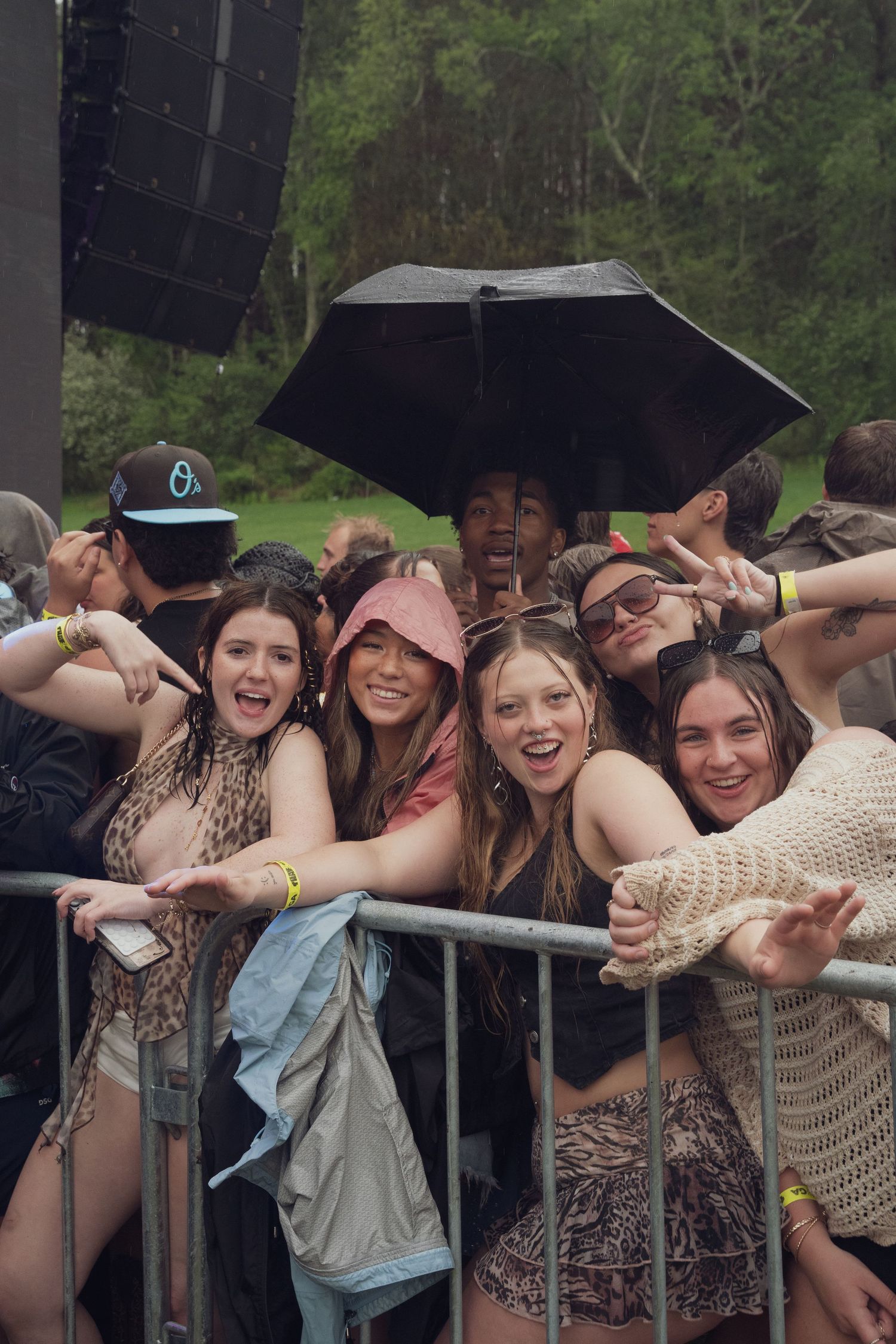 Group of young female festival fans smiling under umbrella at barricade.