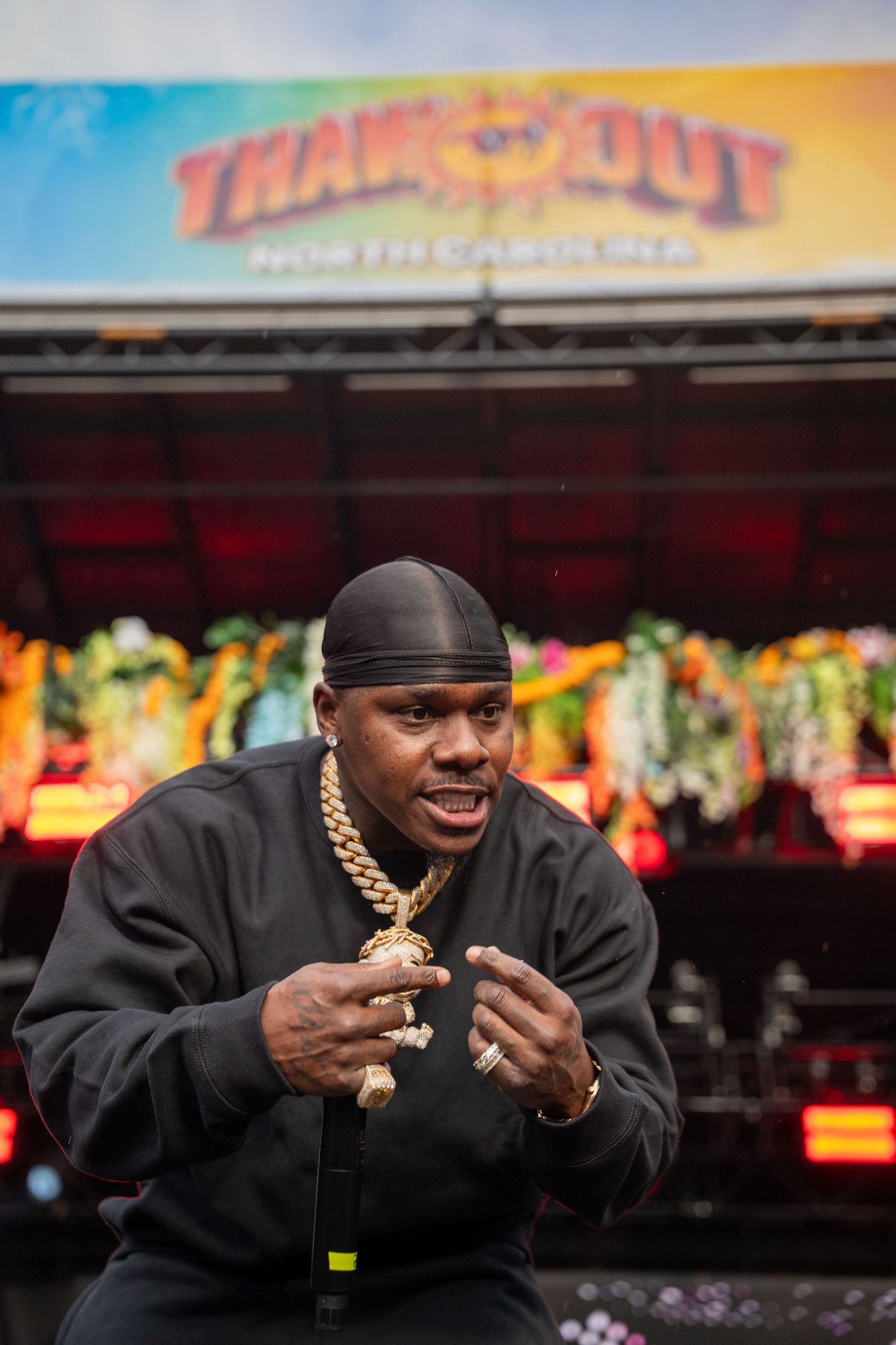Male rapper in black outfit with gold chain crouching on stage at Thank You Out festival event.