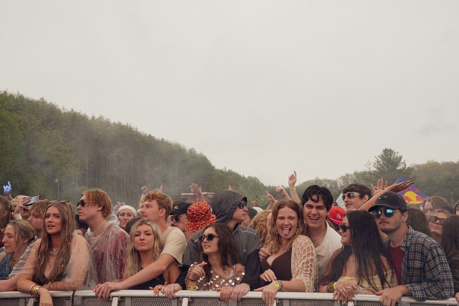 Crowd of festival-goers leaning on barrier at outdoor music festival on overcast day.