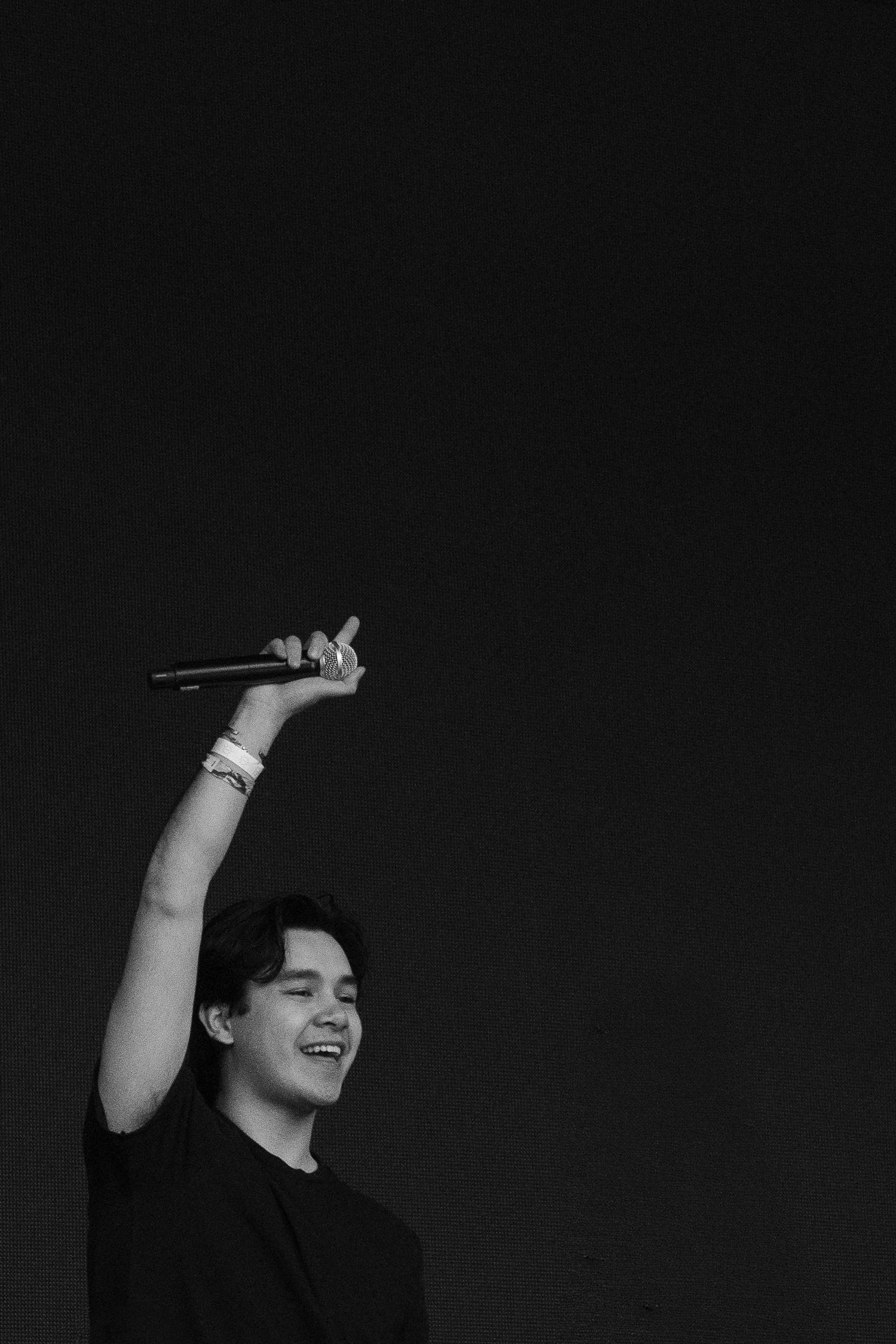 Black and white photo of smiling male performer holding microphone above head on stage.