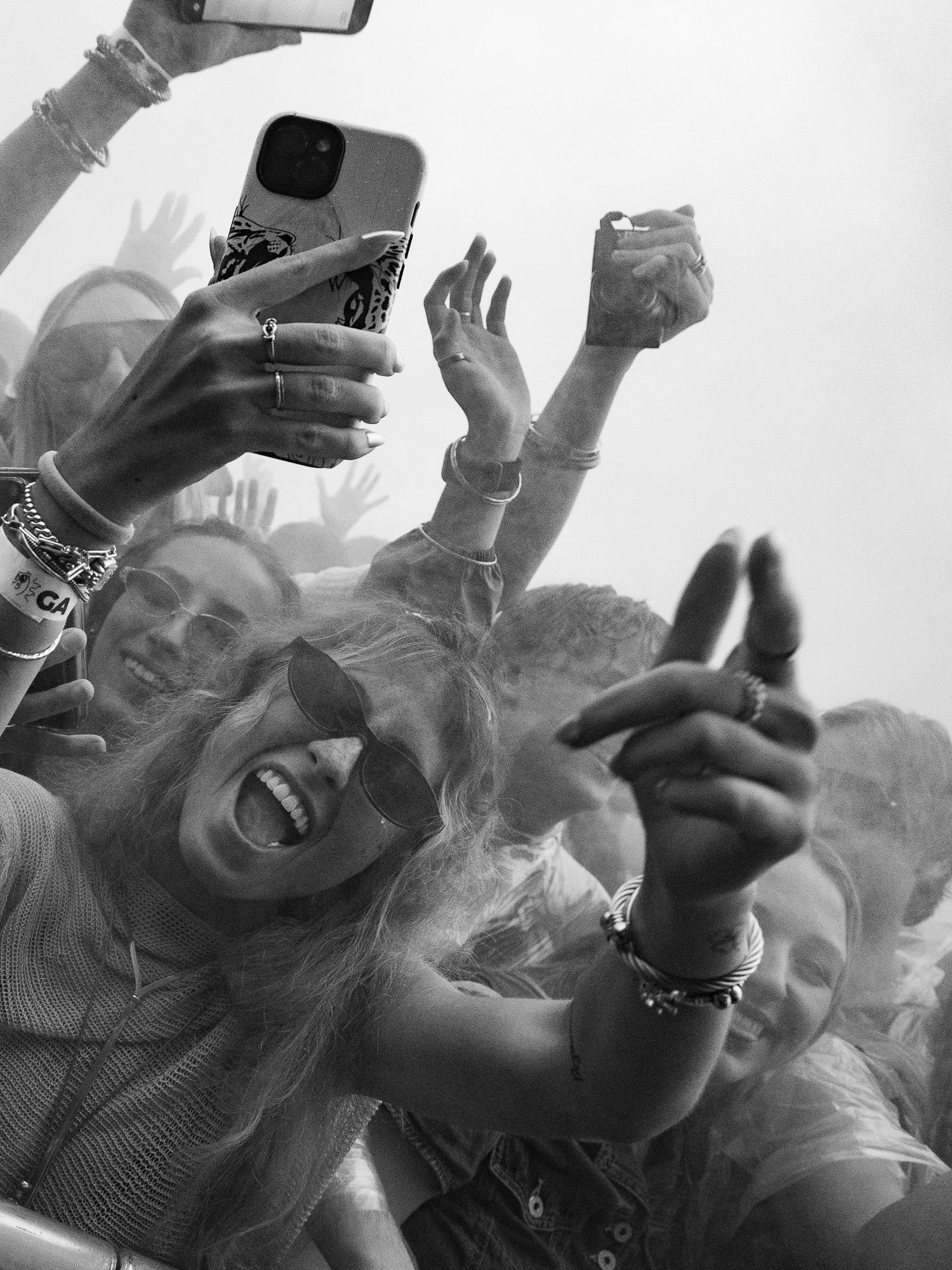 Black and white photo of excited festival crowd with hands raised and phones out.