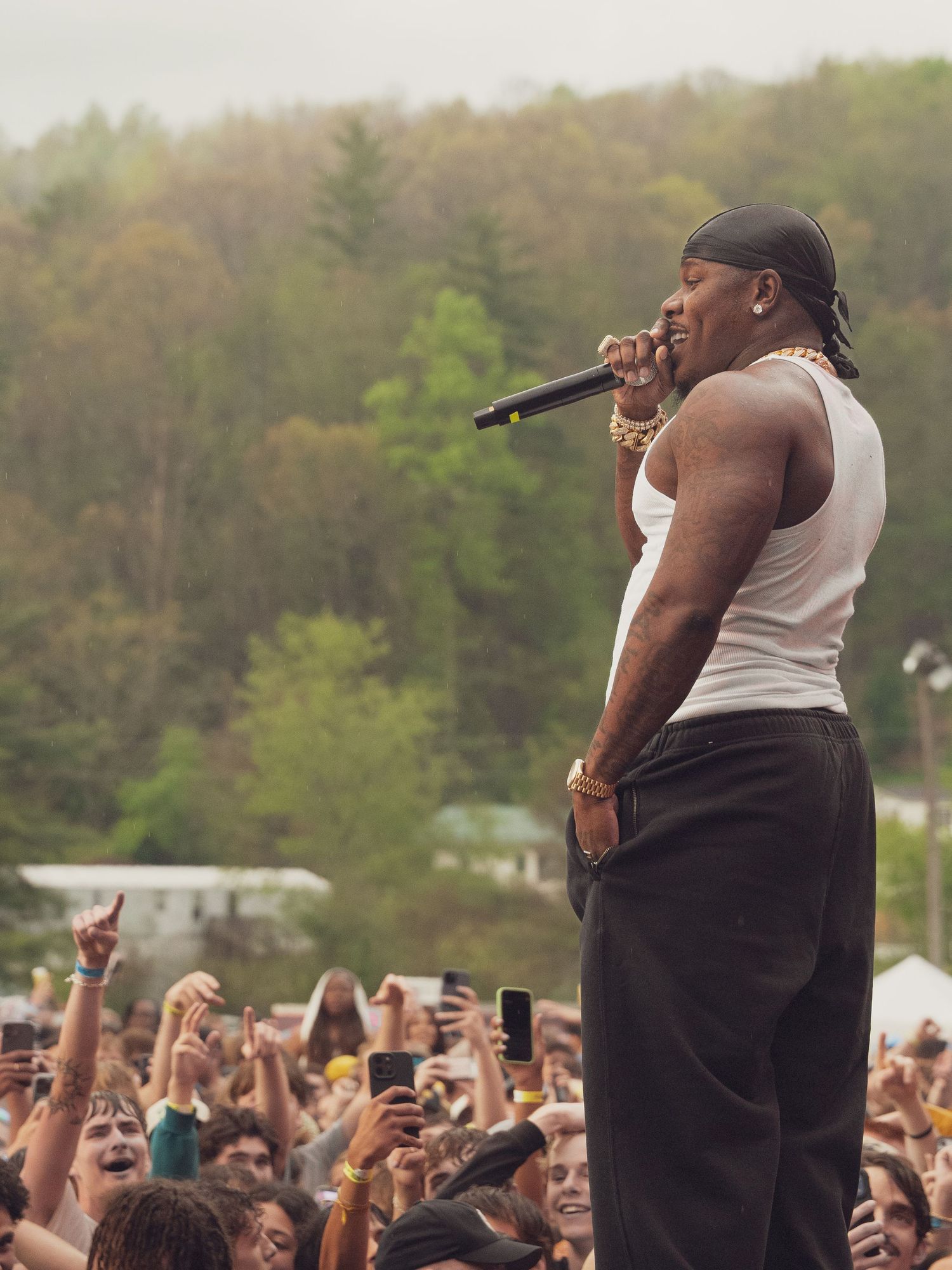 Rapper in white tank top and black pants performs for large outdoor festival crowd.